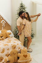 Couple in pajamas standing in a room with gingerbread-themed decor and Christmas tree.
