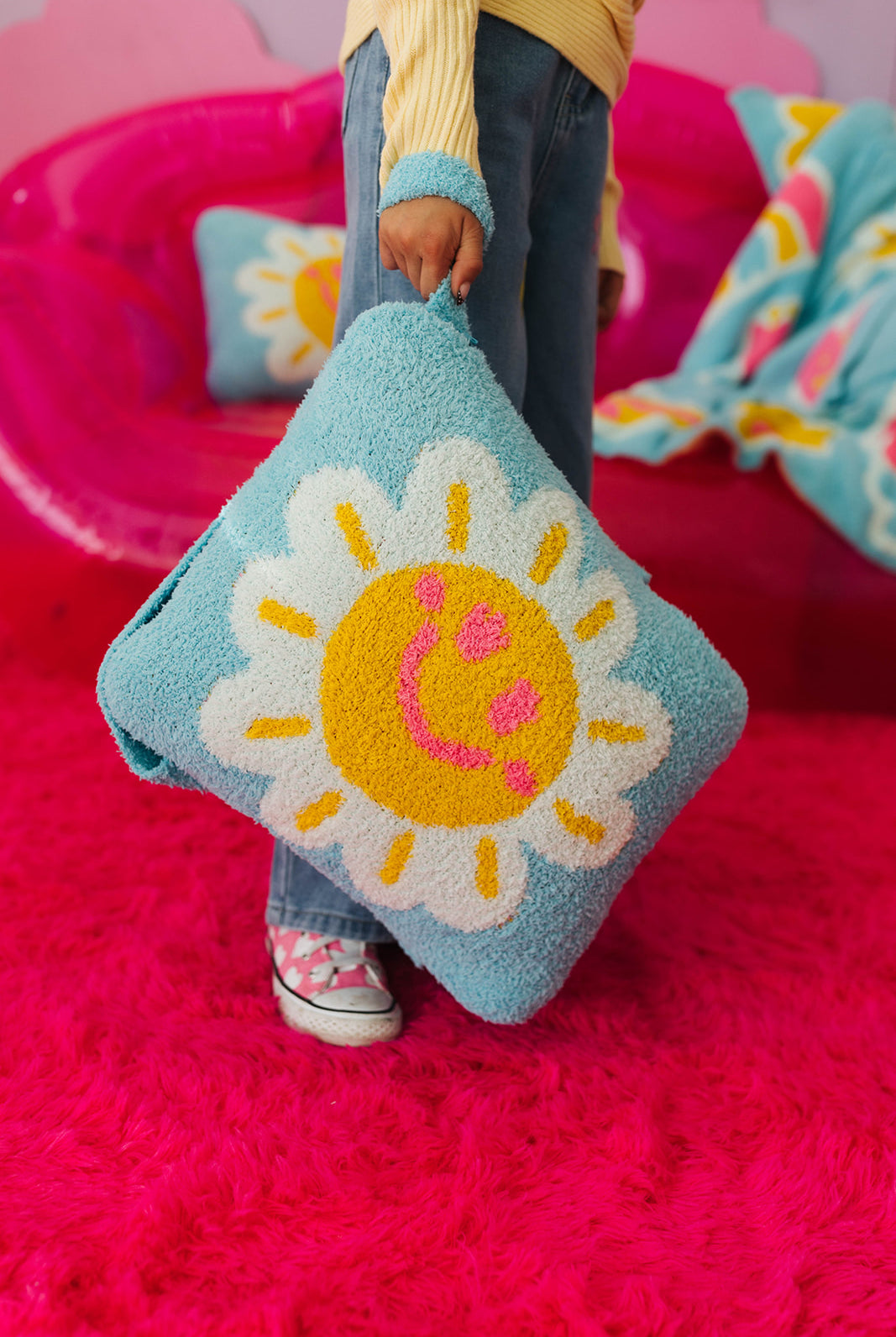 Person holding a blue pillow with a sun design on a pink background