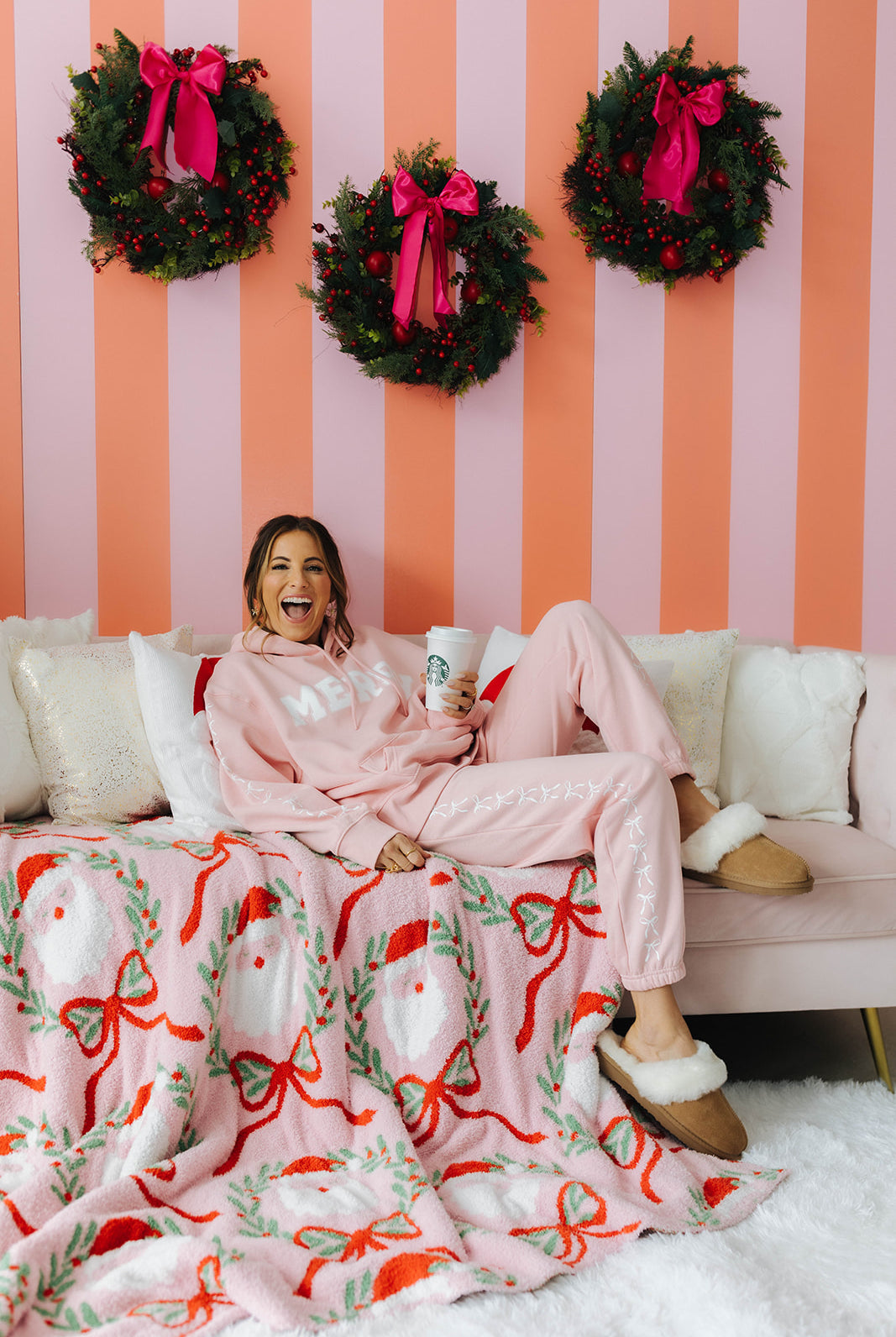 Woman sitting on a couch with a festive blanket and wreaths on a striped wall