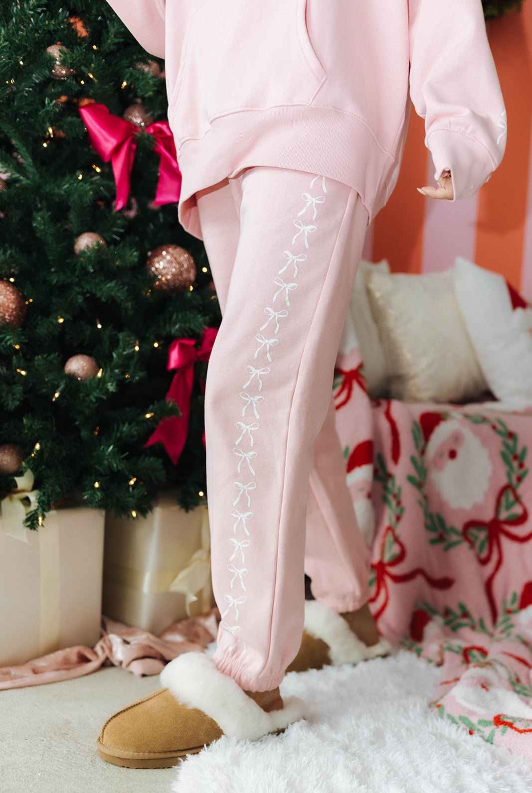 Person wearing pink pants with decorative trim in a festive setting with a Christmas tree and wrapped gifts.