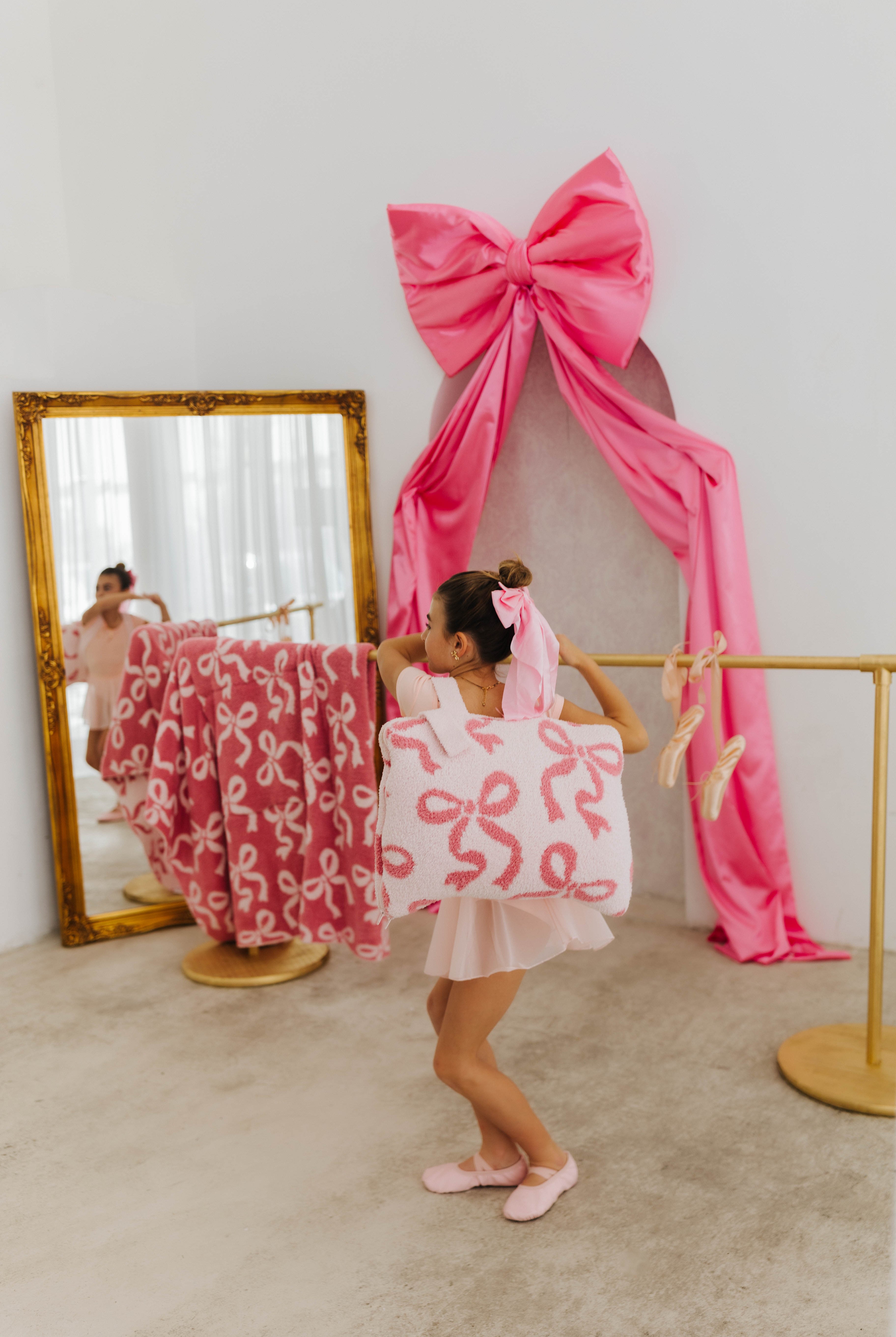 Child in a pink dress with a large bow standing in front of a mirror