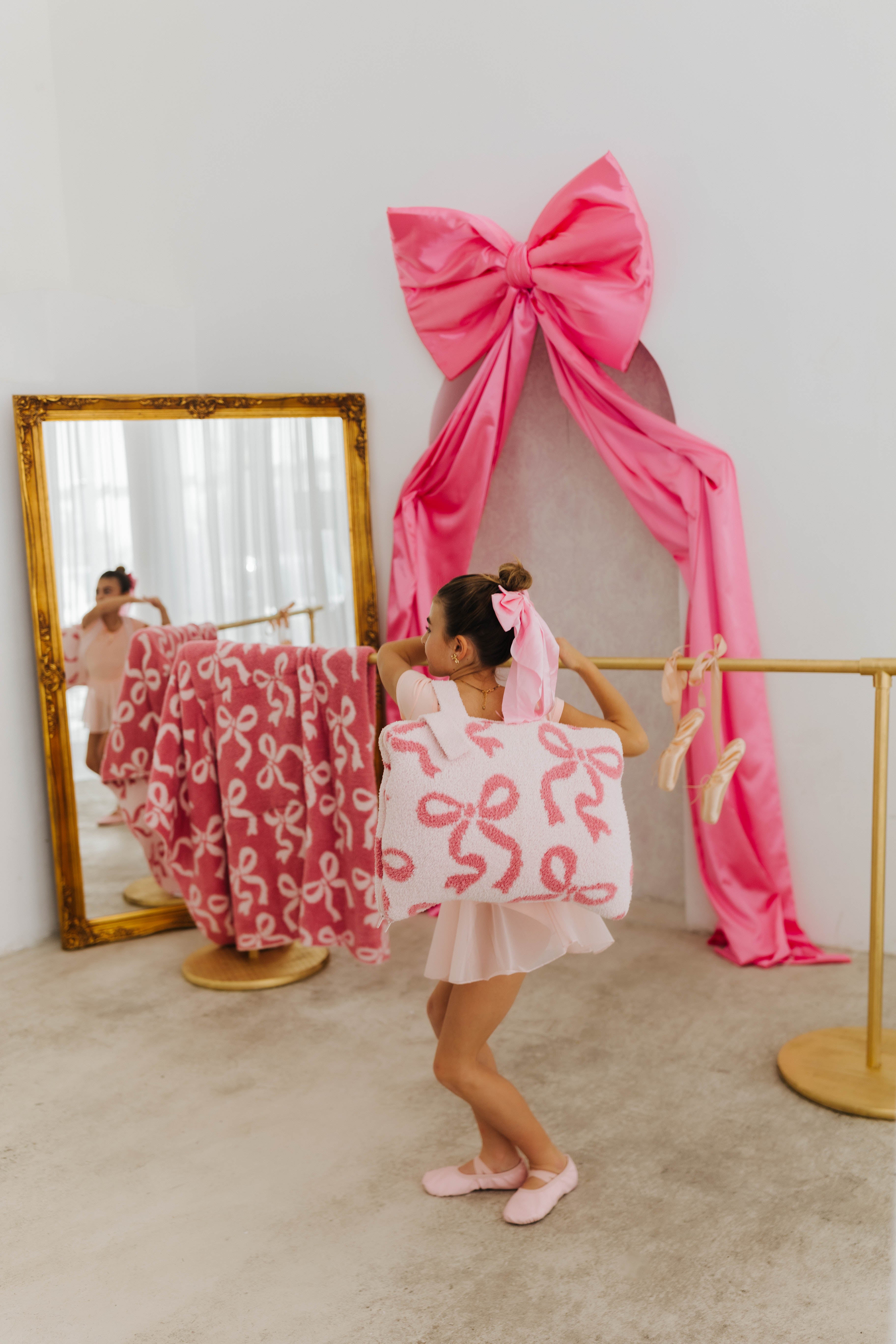 Child in a pink dress with a large bow standing in front of a mirror