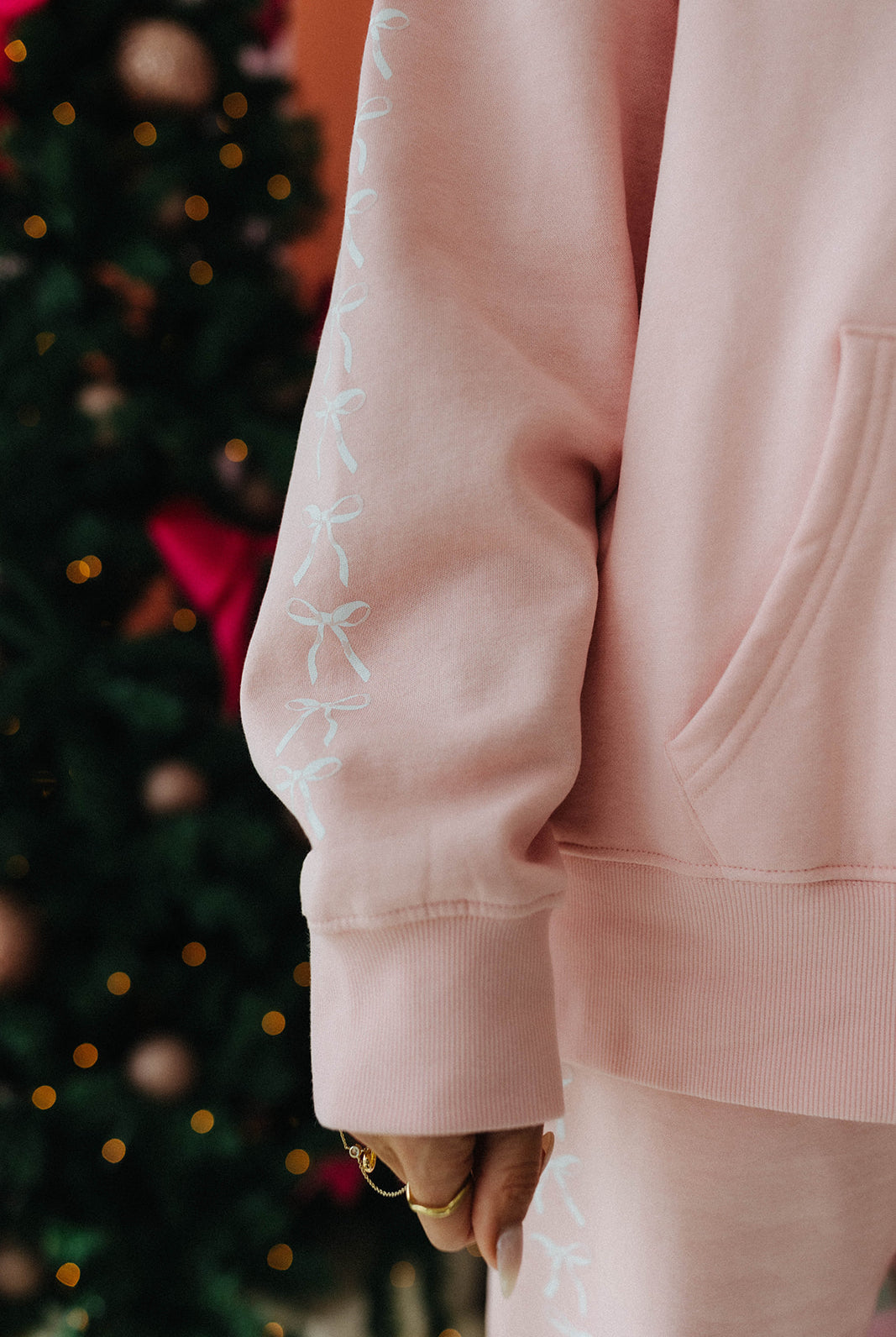 Person wearing a pink outfit with white bow details in front of a decorated Christmas tree.
