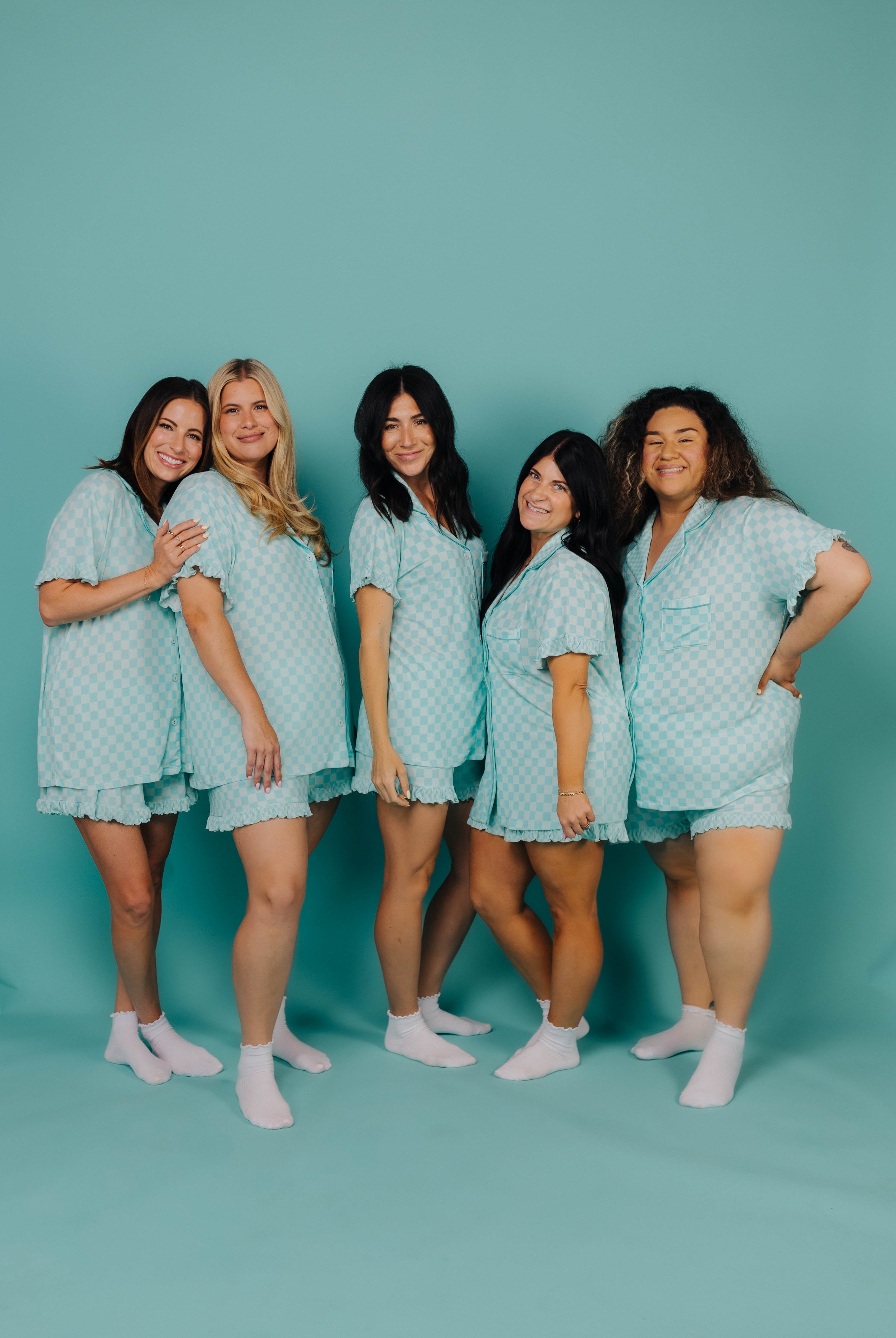 Five women wearing matching teal check outfits against a teal background