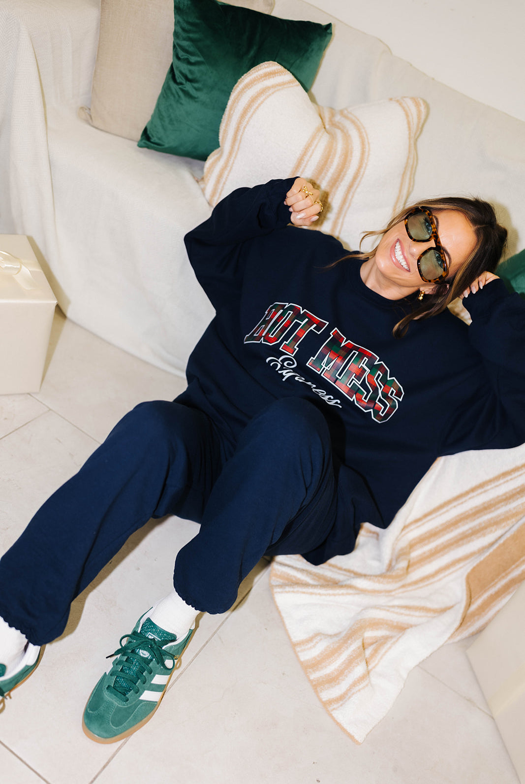 Person wearing a navy sweatshirt with text, sitting on a couch with pillows.