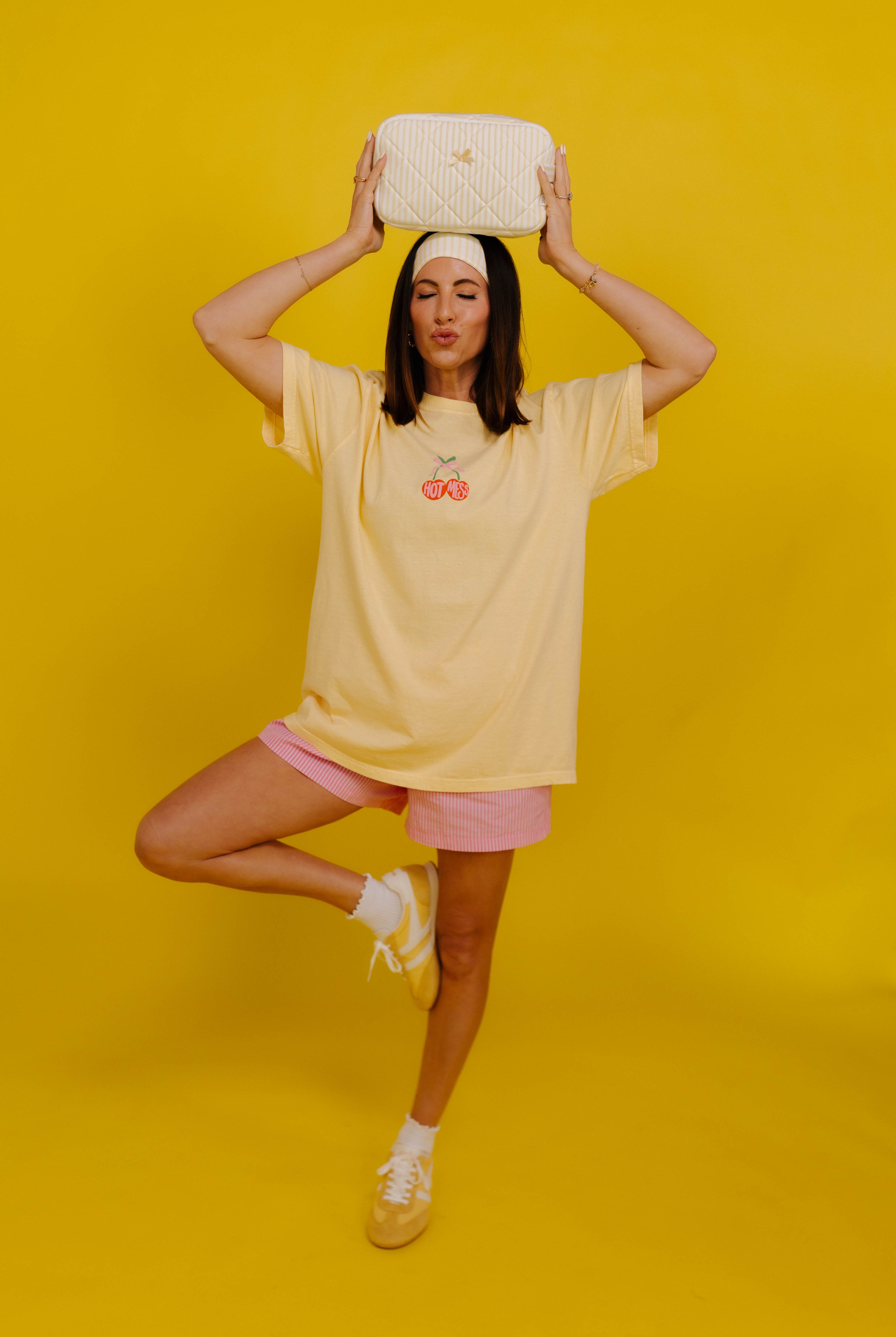 Person wearing a yellow oversized t-shirt and pink shorts on a yellow background with bag on her head
