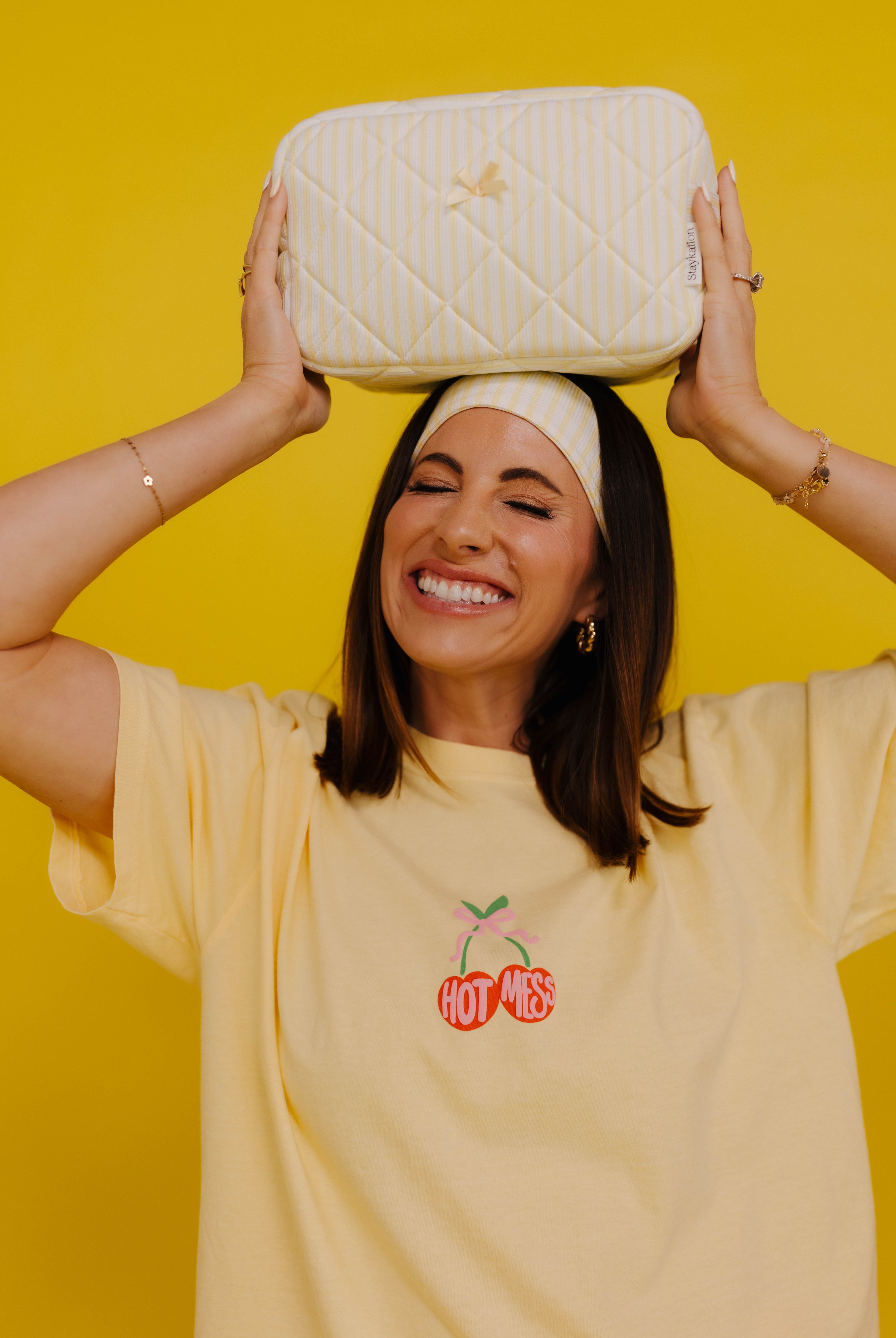 Woman holding a white quilted bag above her head against a yellow background
