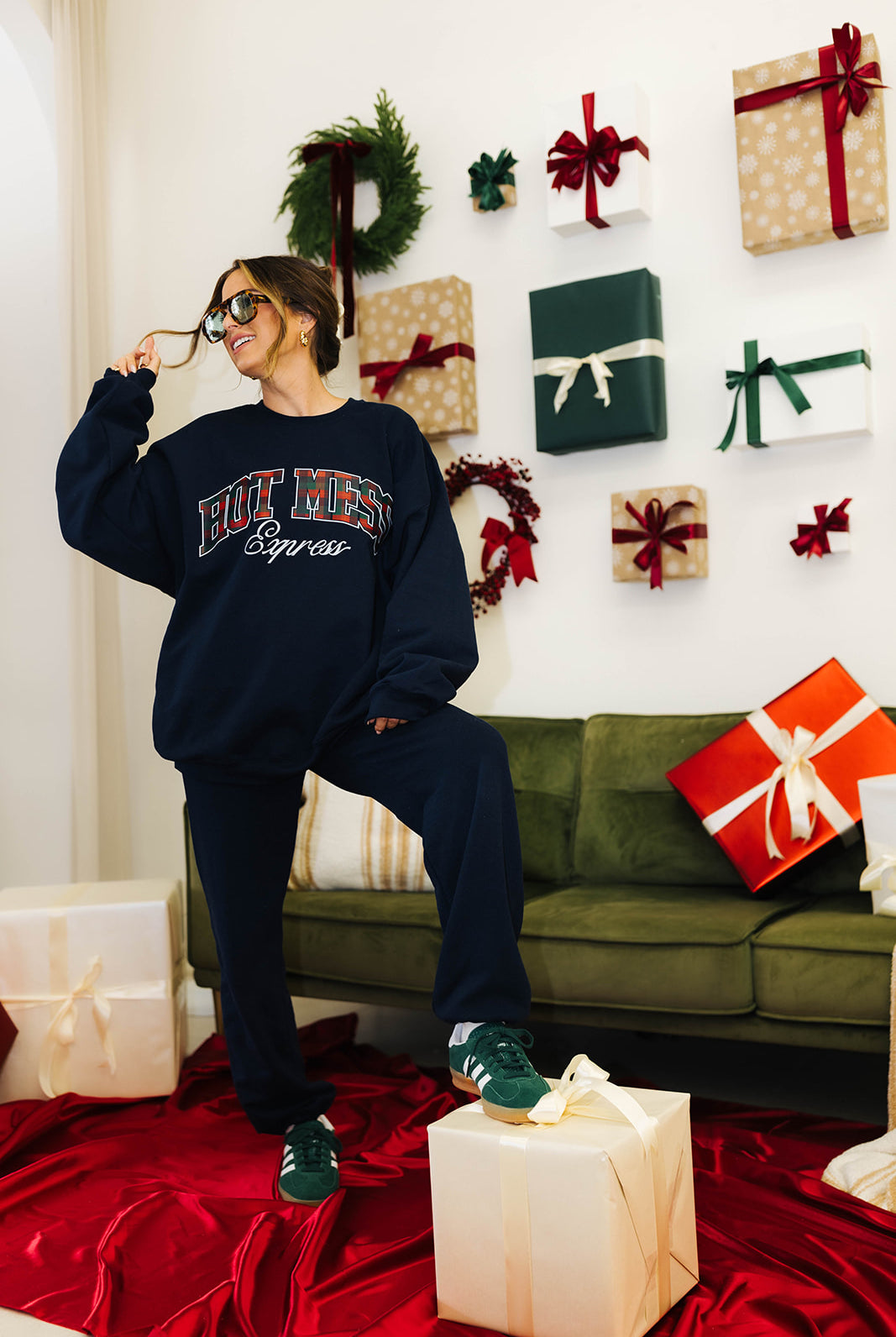 Person wearing a navy sweatshirt with text, sitting on a green couch surrounded by Christmas presents.
