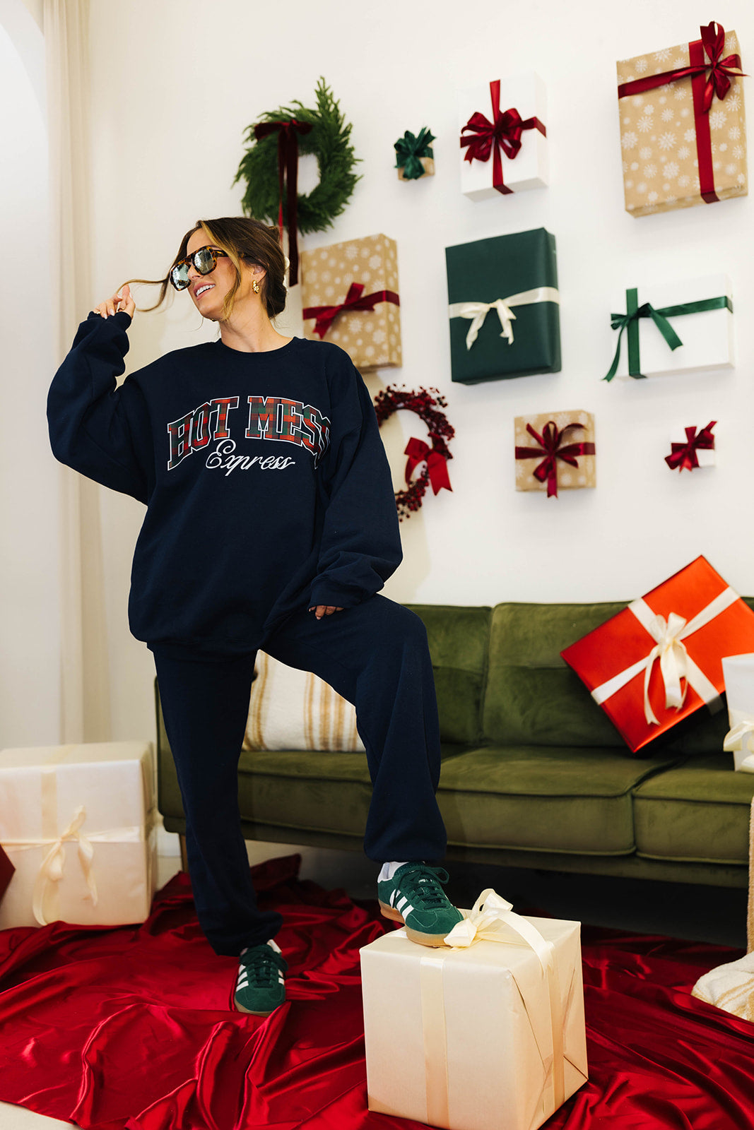 Person wearing a navy sweatshirt with text, sitting on a green couch surrounded by Christmas presents.