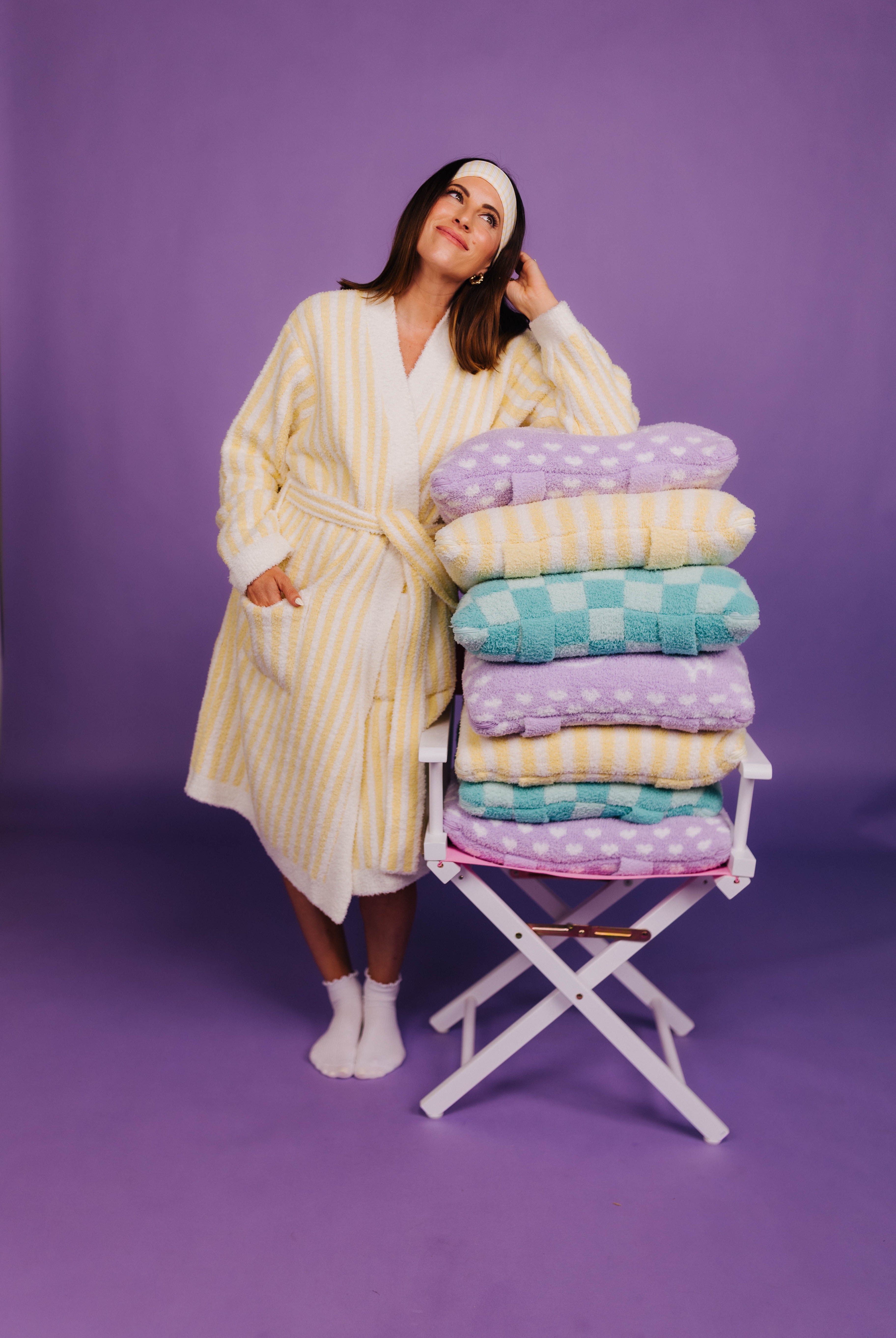 Woman in a yellow robe standing next to a stack of quillows and blankets