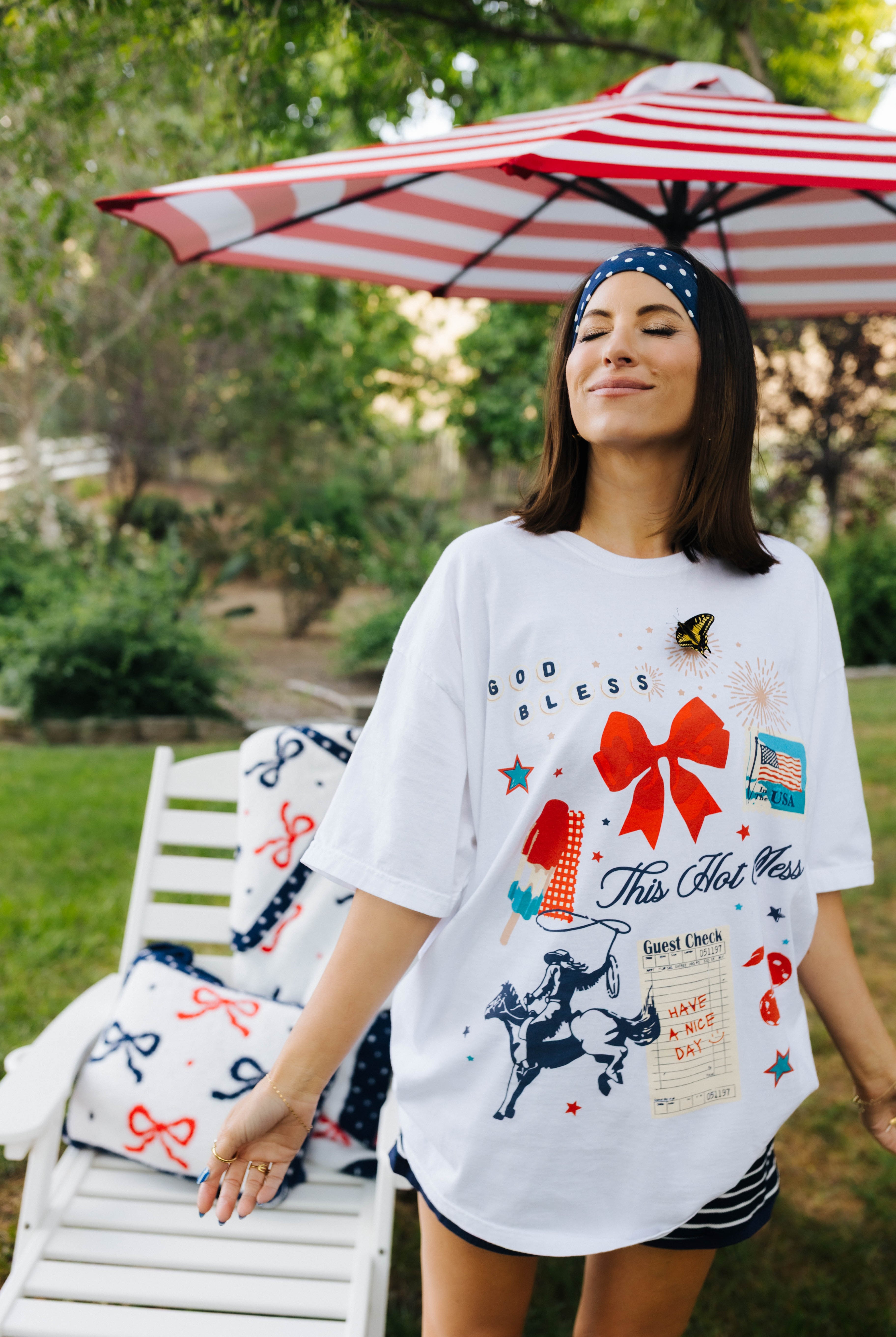 Woman wearing a white graphic t-shirt outdoors with an umbrella in the background