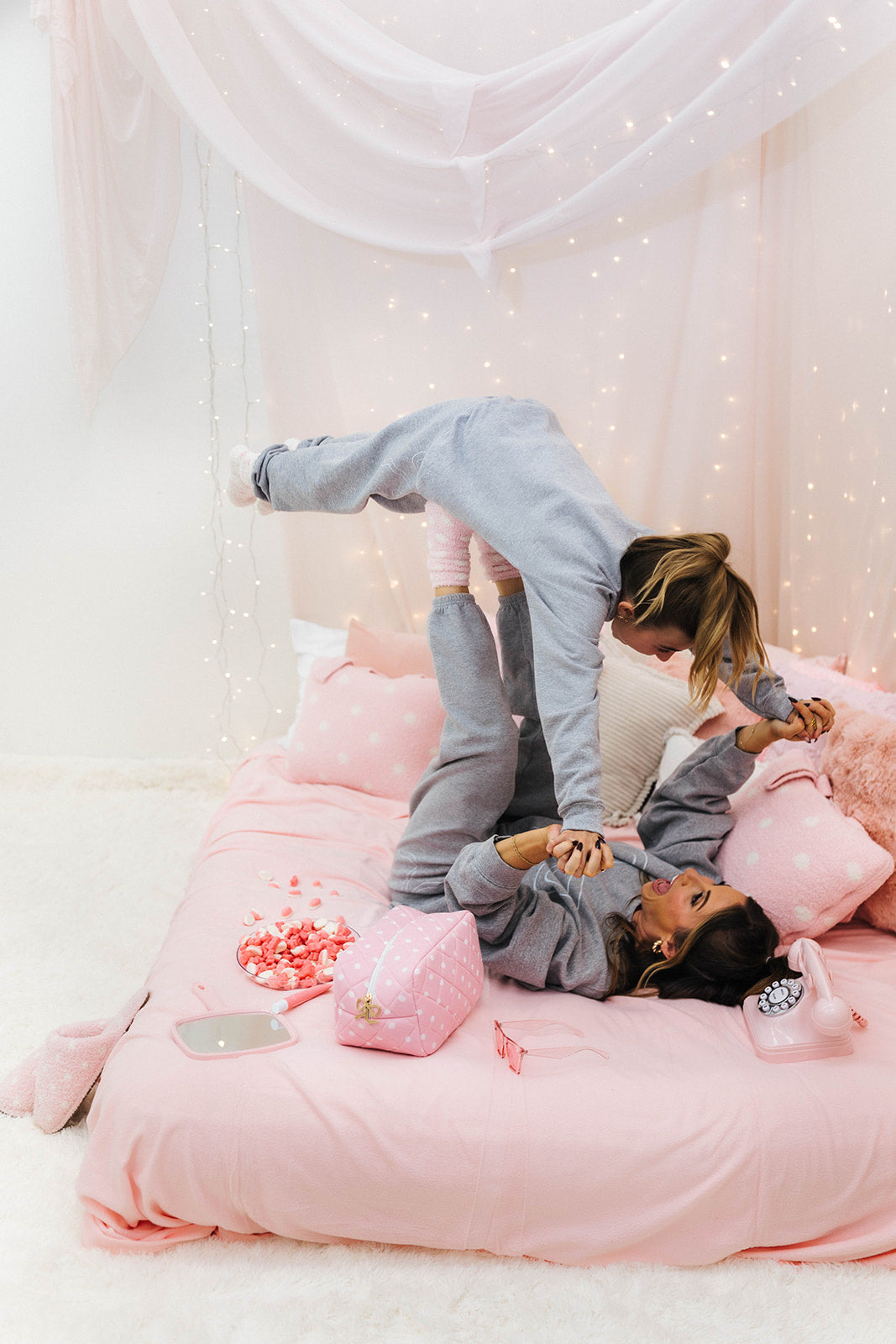 Two people in a playful pose on a bed with pink bedding and decorations.