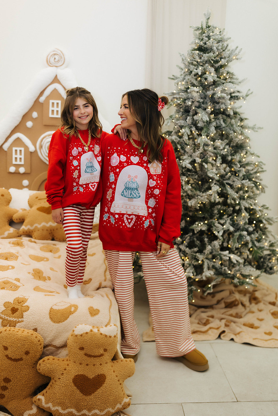Two people wearing matching red sweaters with Christmas designs in a festive room with a decorated tree and gingerbread cookies.