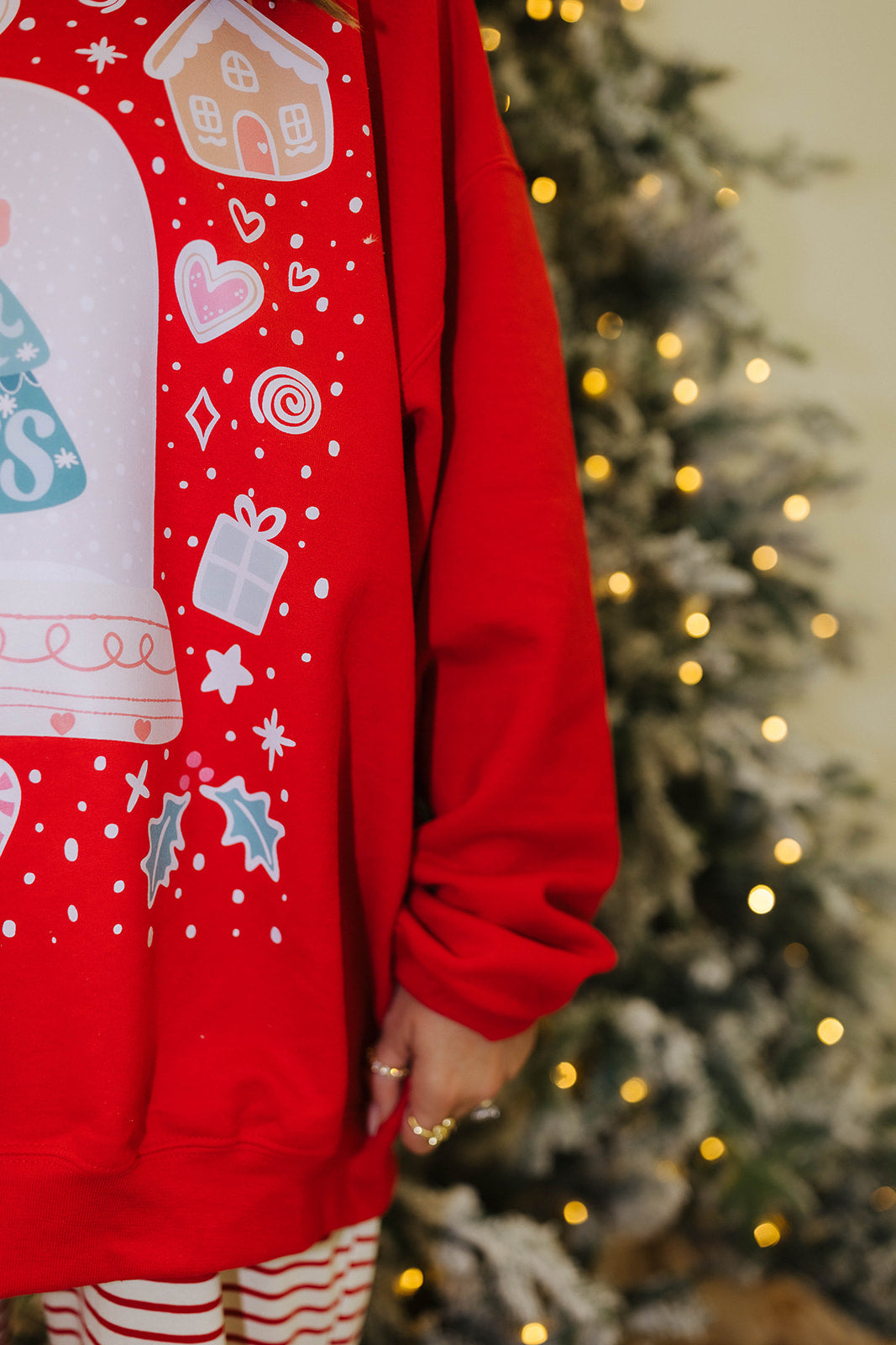 Red hoodie with festive designs worn by a person, Christmas tree in the background