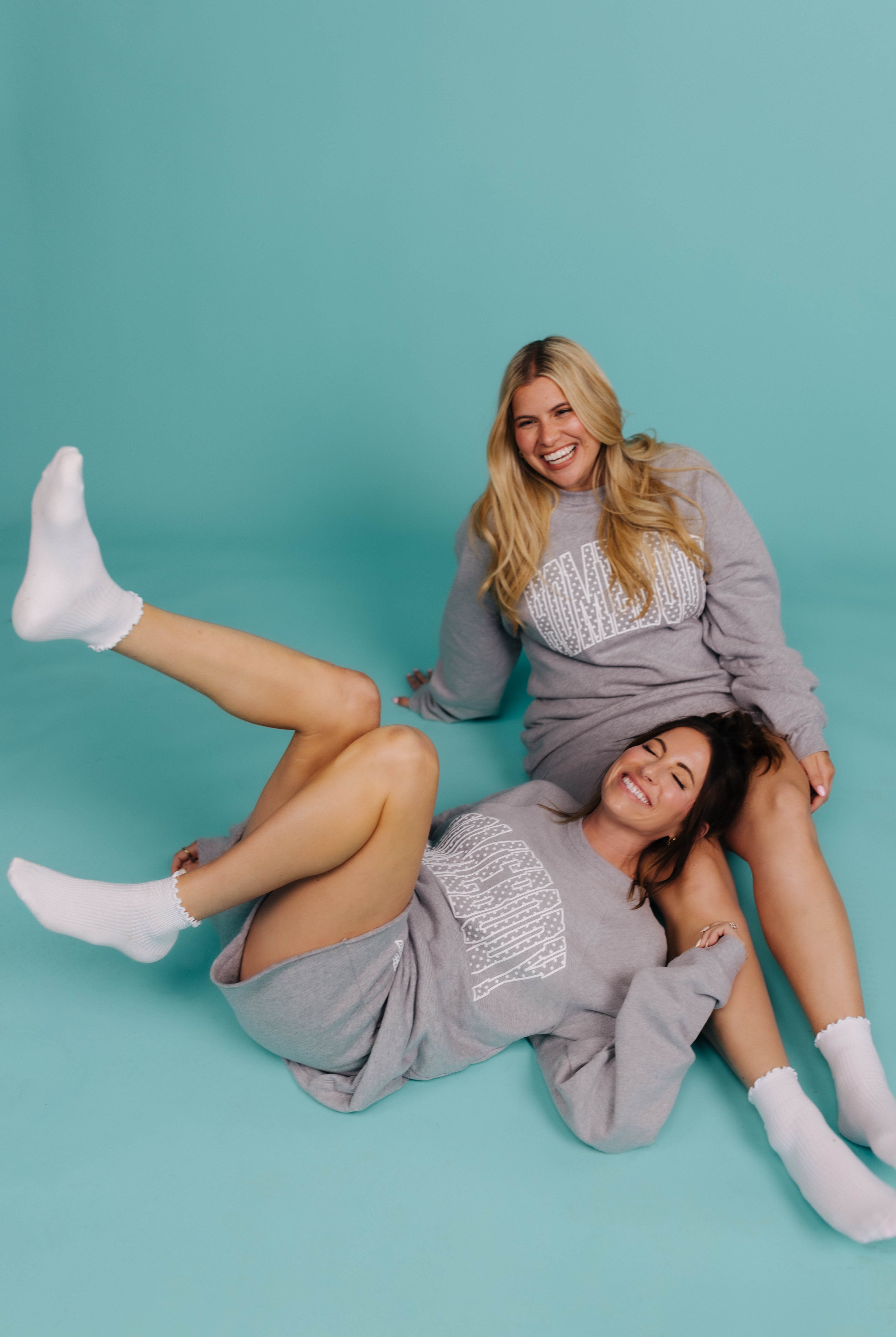 Two women in gray sweatshirts posing against a teal background
