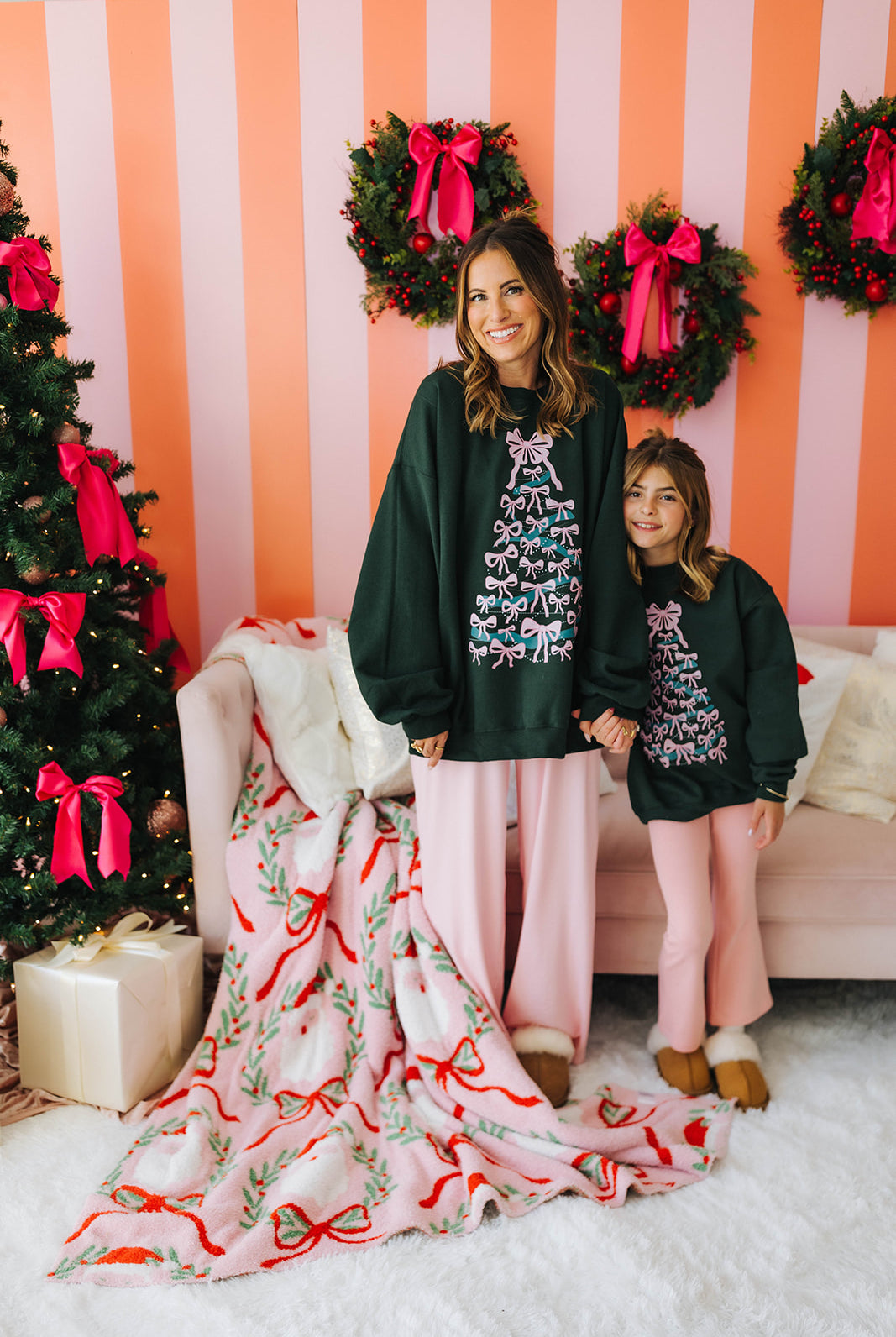 Two women in matching outfits standing in a festive room with Christmas decorations.