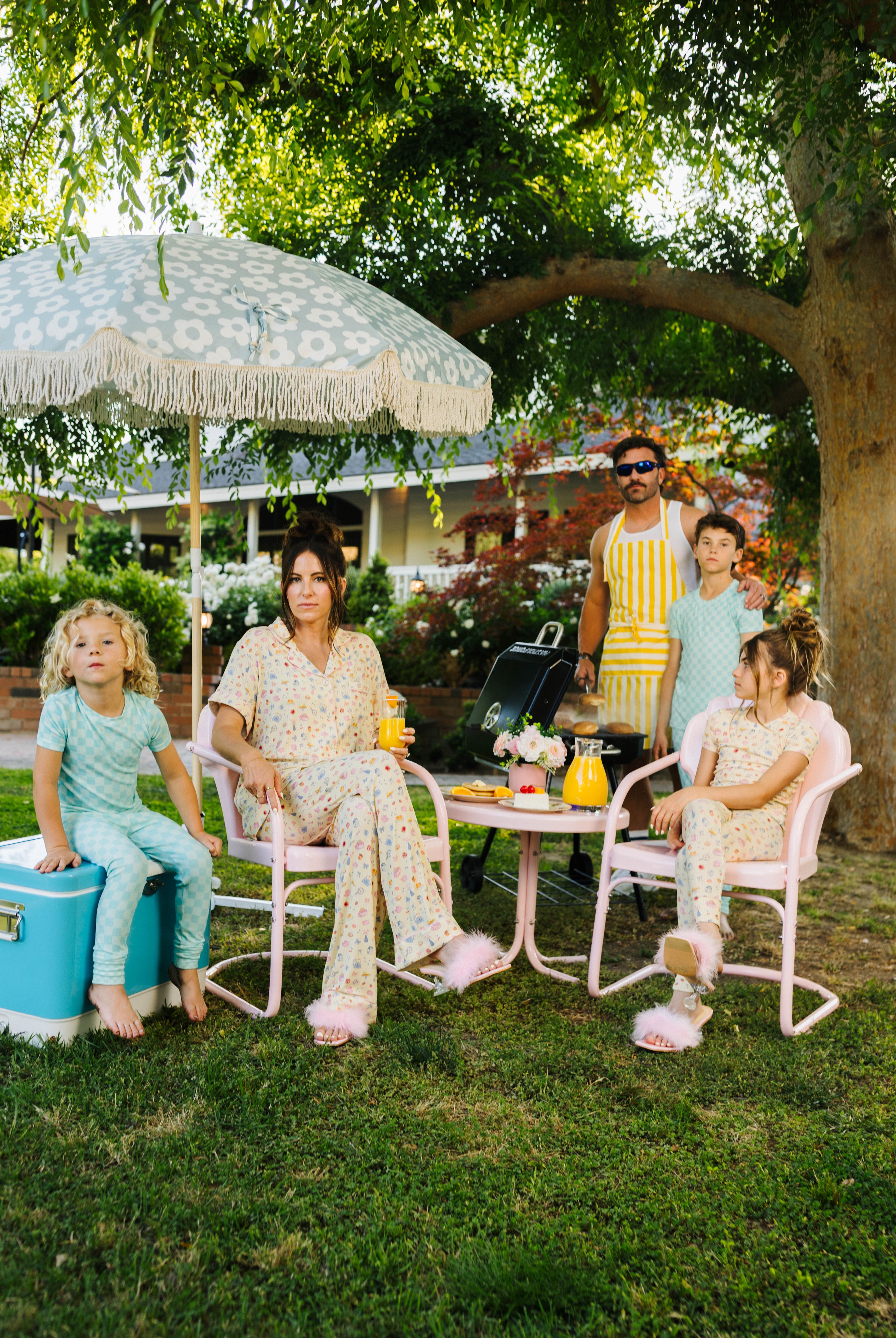 Family of five sitting outdoors under a large umbrella with a garden setting.
