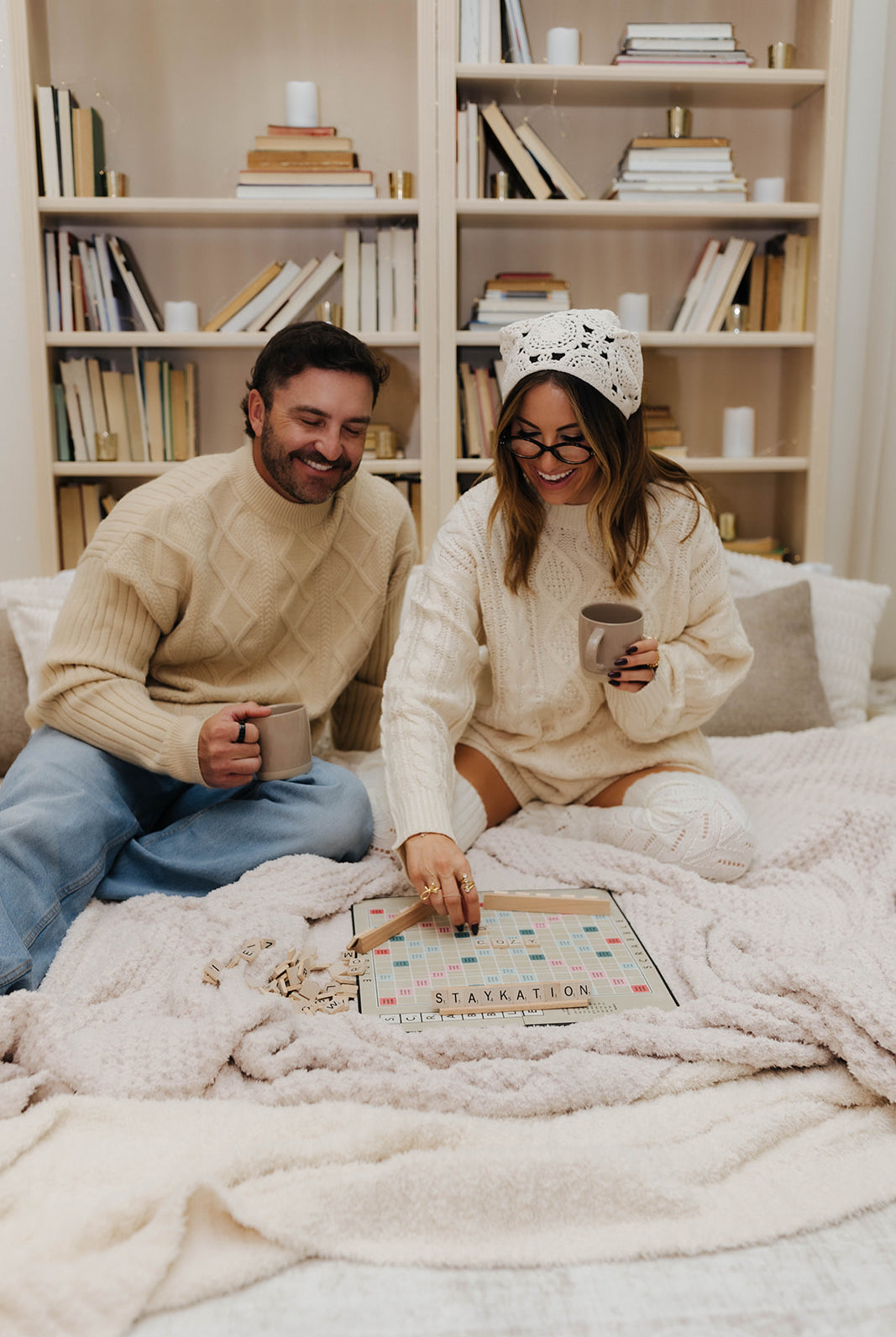 Man and woman sitting on blankets playing a board game together, surrounded by books on shelves.