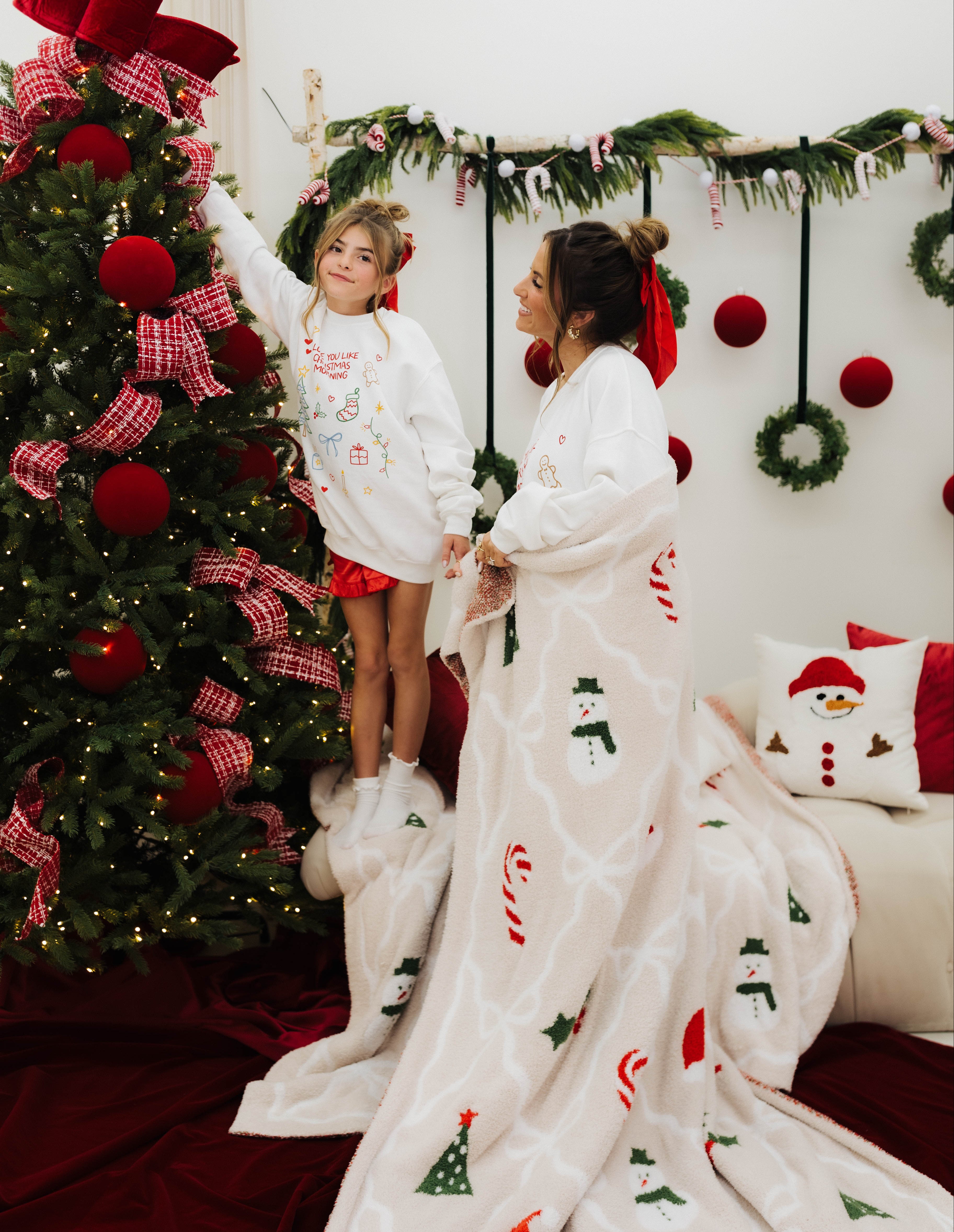 Woman and child in matching Christmas-themed outfits standing in front of a decorated Christmas tree.