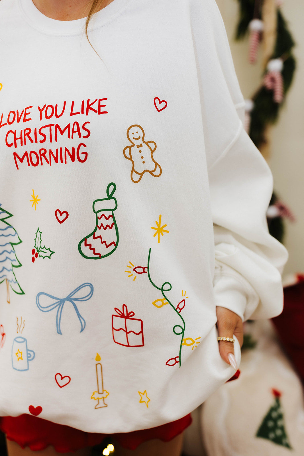 White sweatshirt with Christmas-themed designs and text, worn by a person.