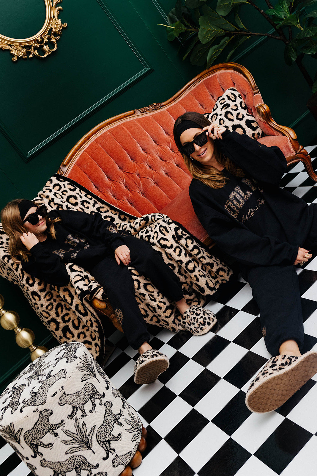 Two women sitting on a red couch with leopard print accents in a stylish room.