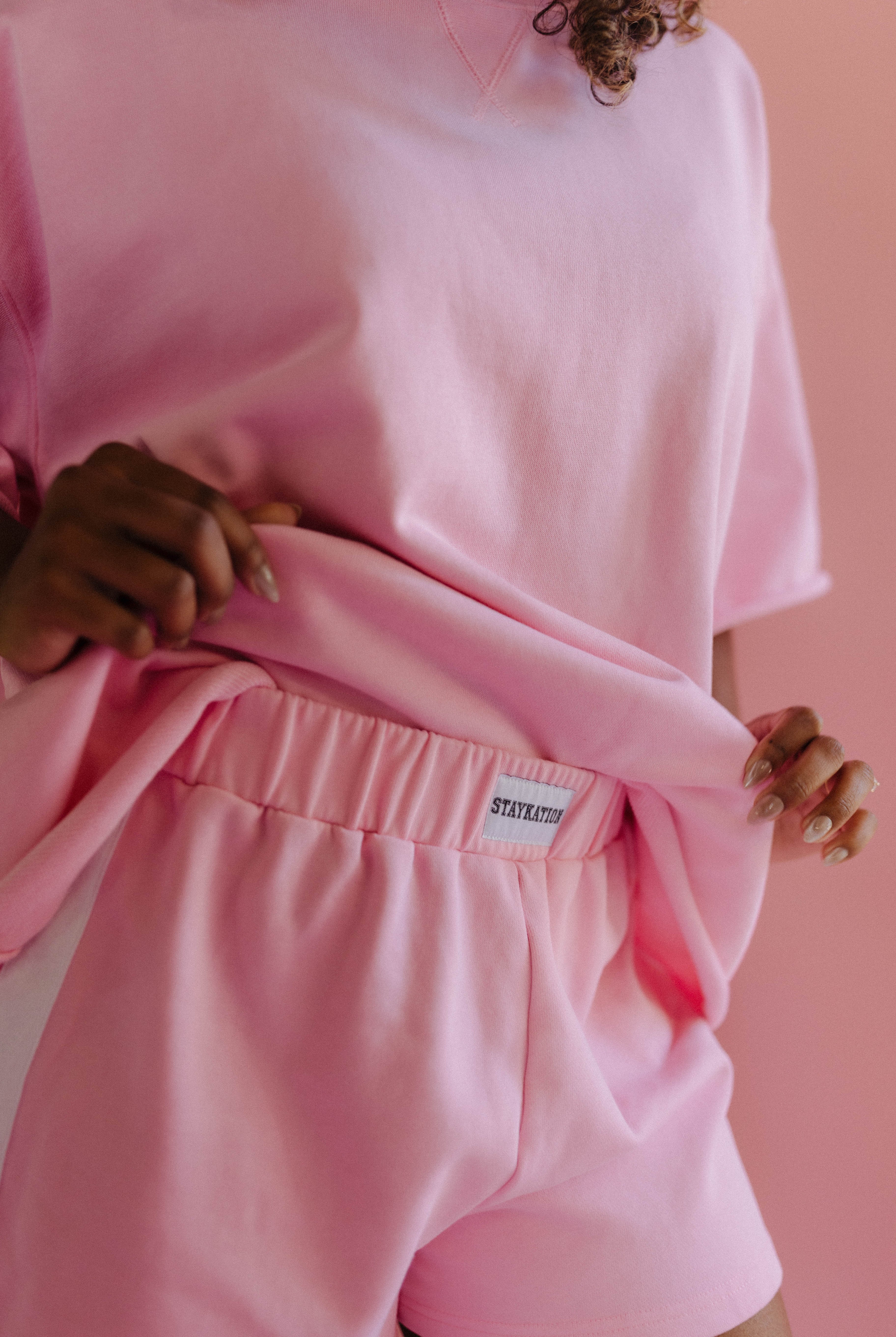 Person wearing a pink outfit with a Staykation label against a pink background