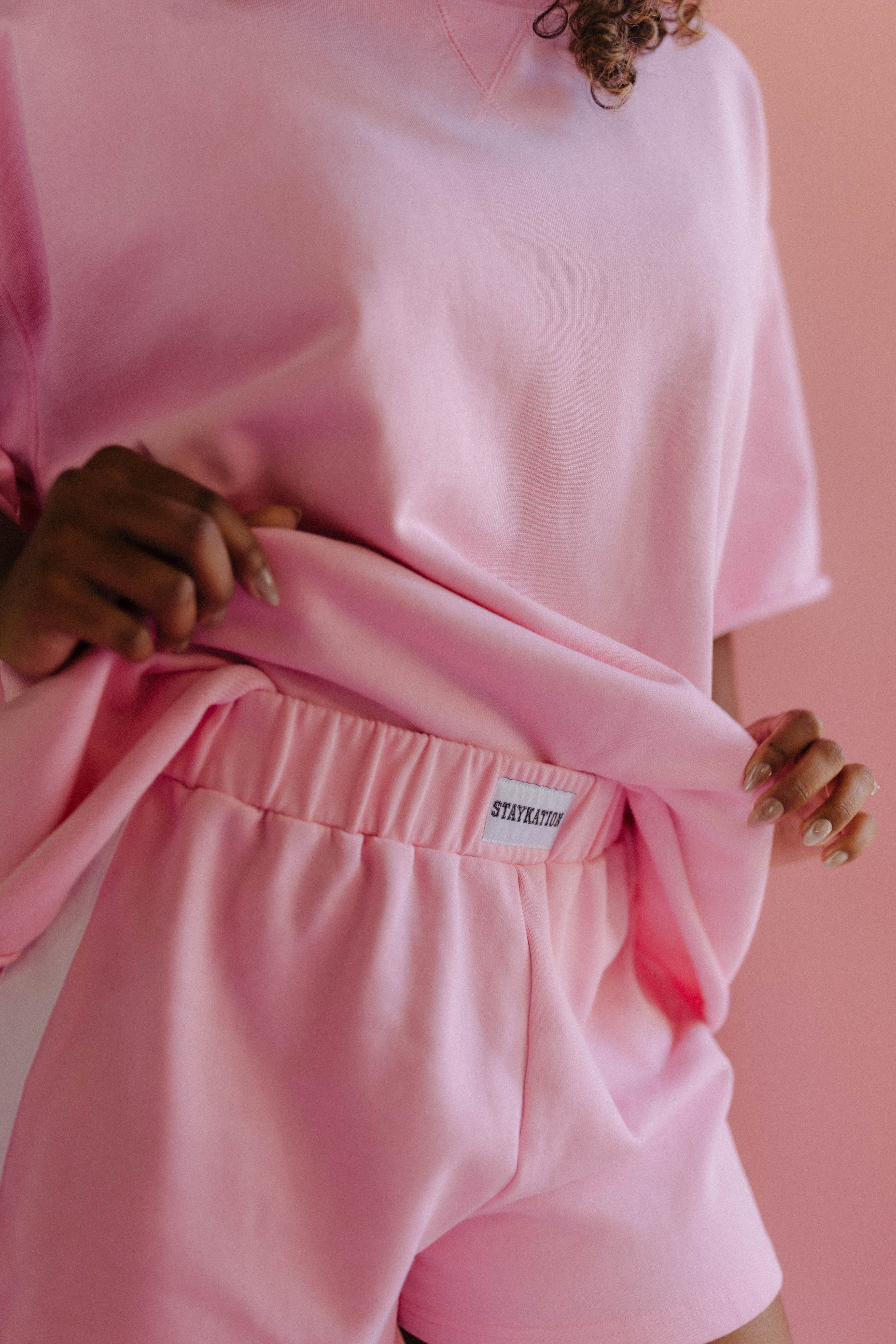 Person wearing a pink outfit with a Staykation label against a pink background