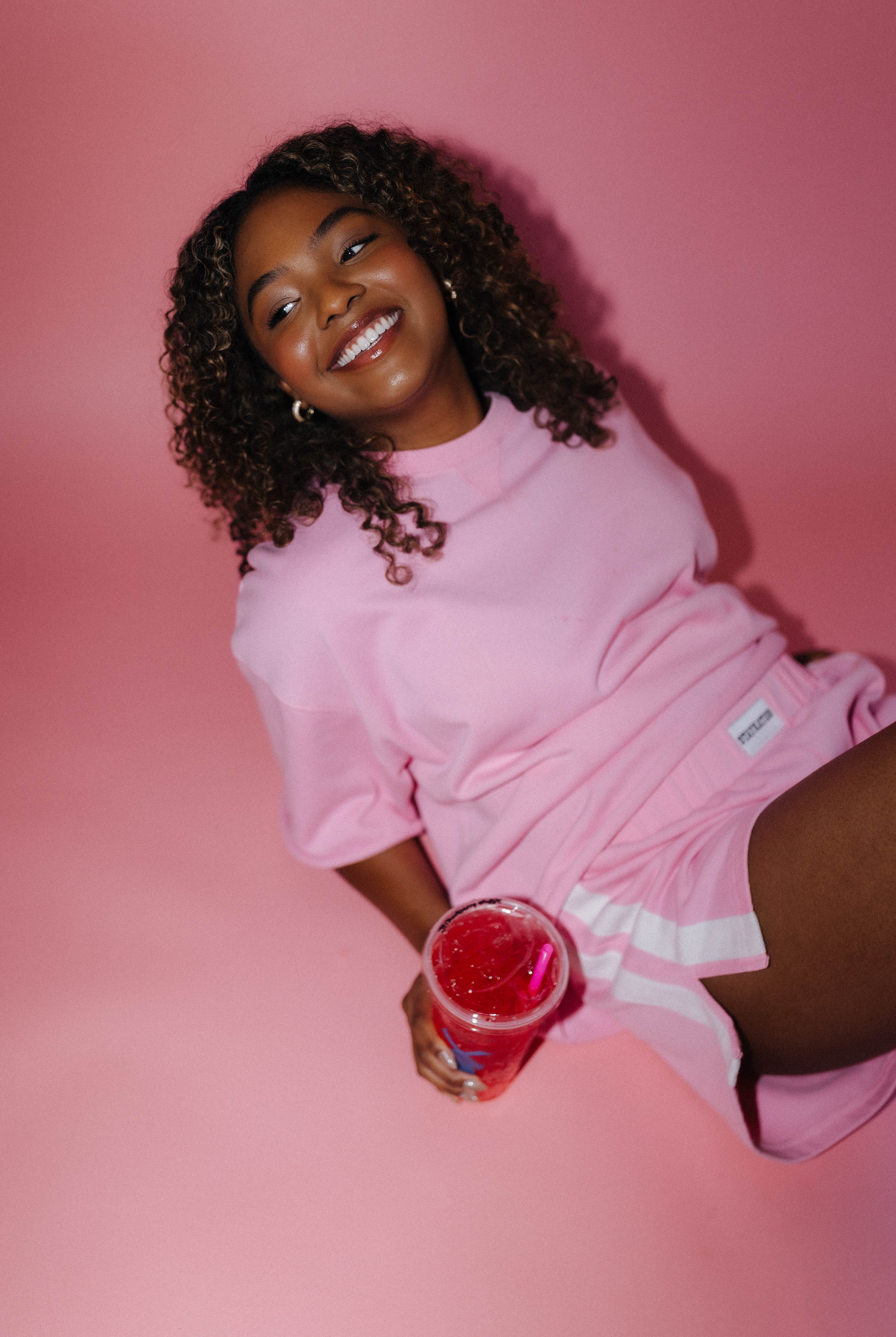 Woman in pink outfit holding a drink against a pink background