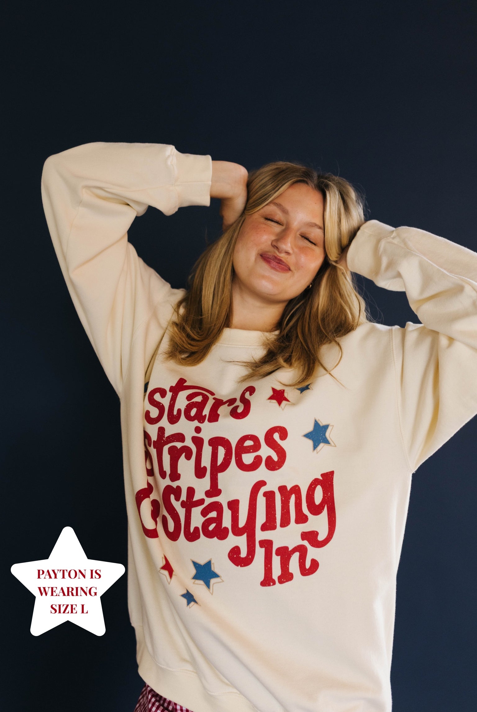 Person wearing a sweatshirt with 'stars stripes & staying in' text on a dark background