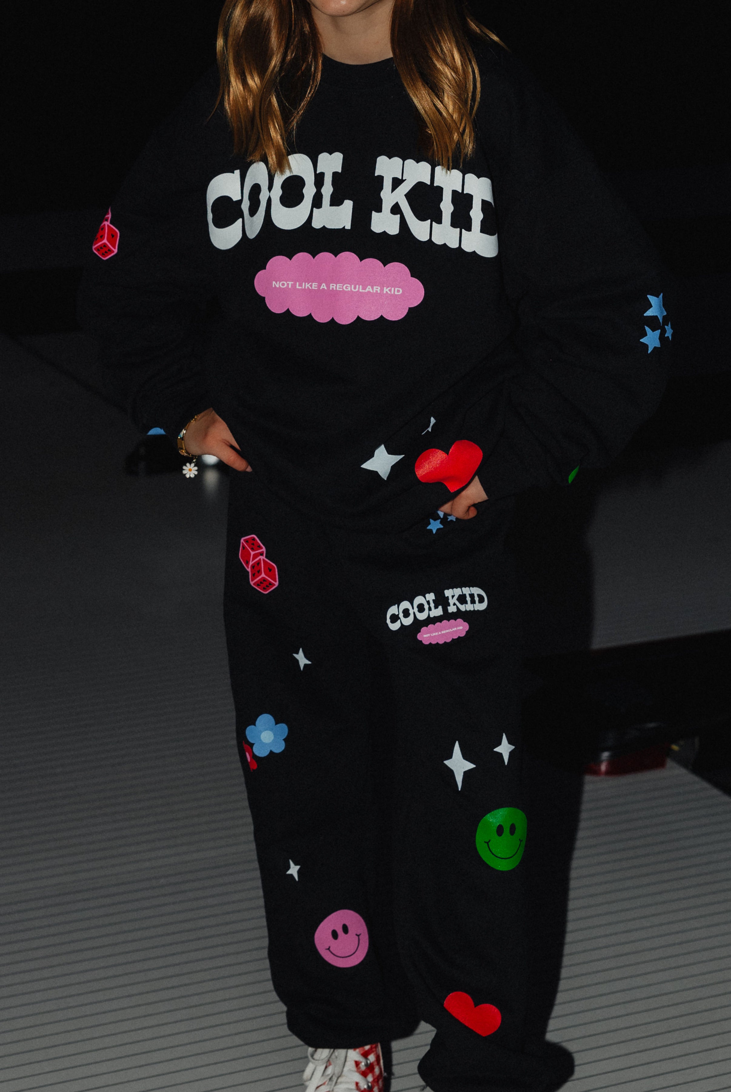 Sweatpants showing the cool kid logo and the not like a regular kid text along with the flowers, dice, smiley, hearts and flowers.