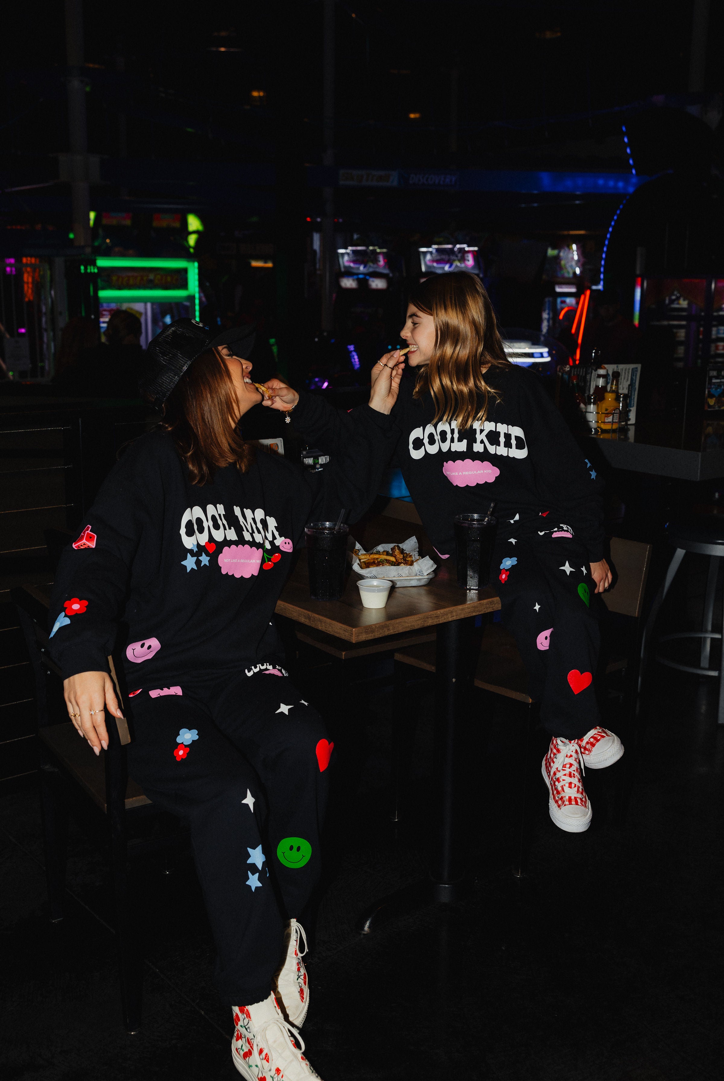 Krista sharing fries with kolly while sitting at the table showign their matching sweatsets.