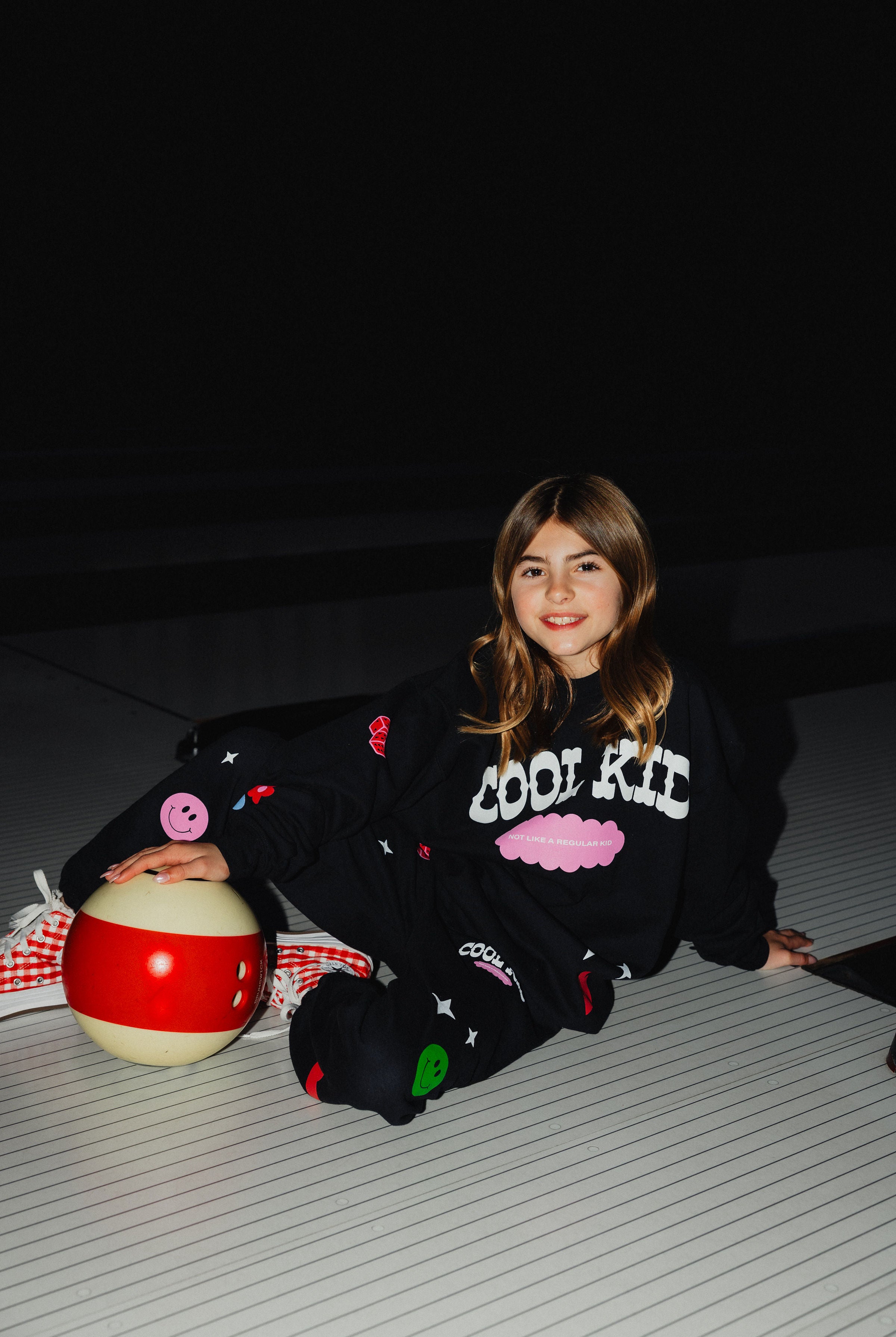 Kolly sitting on the ground of the bowling alley with the bowling ball.