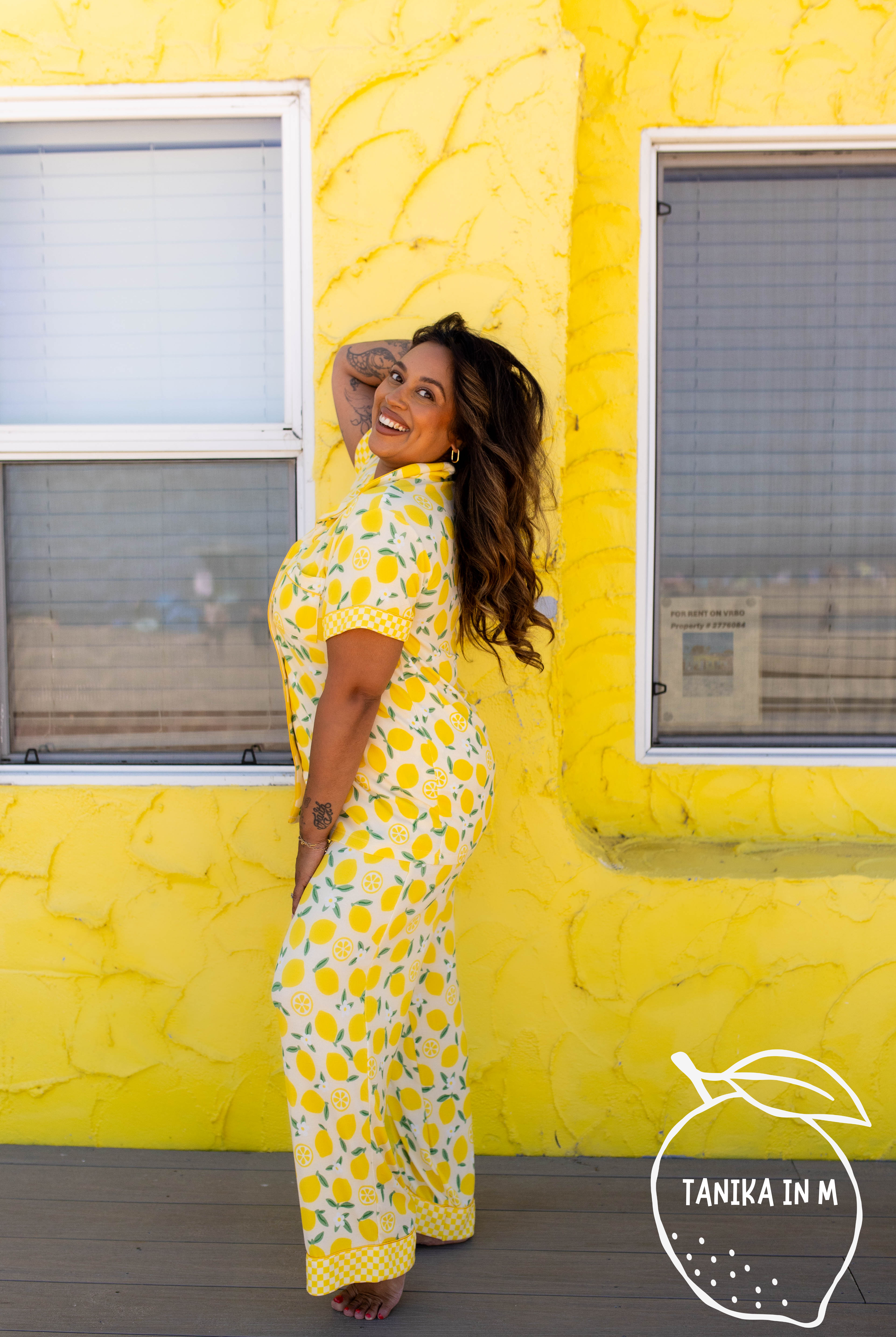 A woman posing in a yellow and white lemon-print pj in front of a bright yellow textured wall.