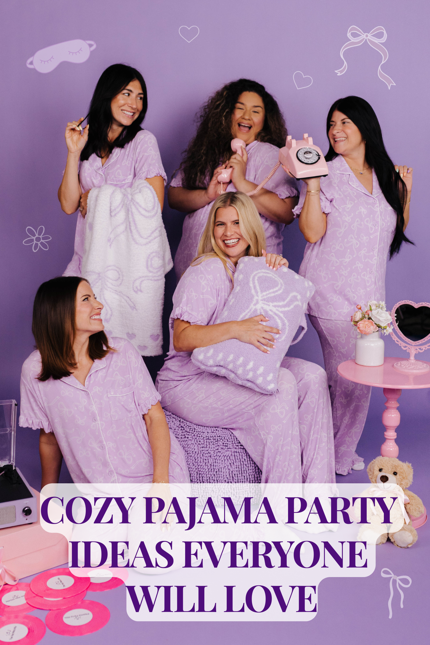Women in matching lavender pajamas posing for a cozy pajama party with blankets, pillows, and girls night accessories.