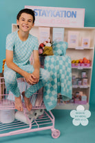 Child in matching teal pajama set sitting on a pink cart with 'STAYKATION' sign in the background.