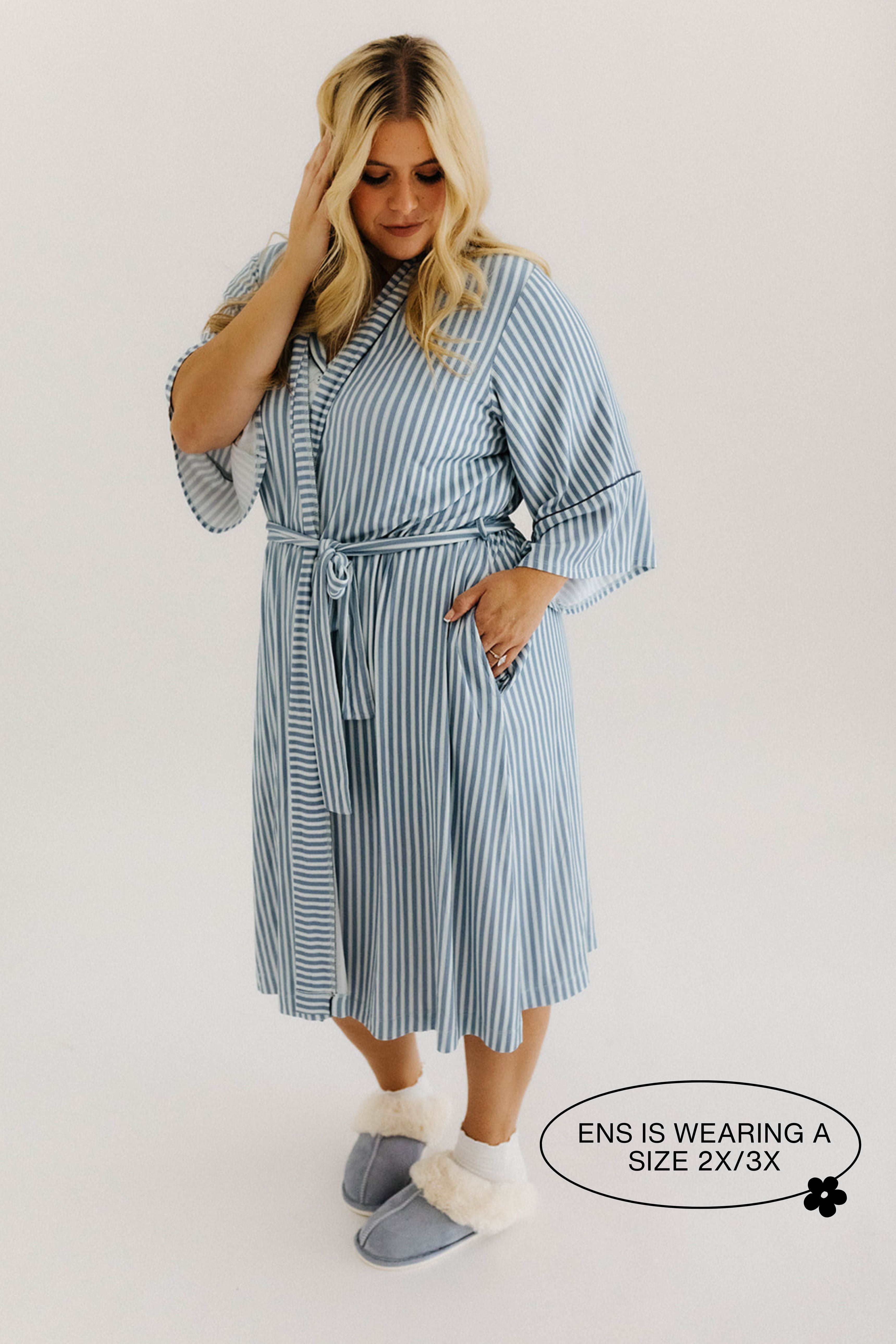 model smiling looking down with hand in pocket wearing blue striped robe 