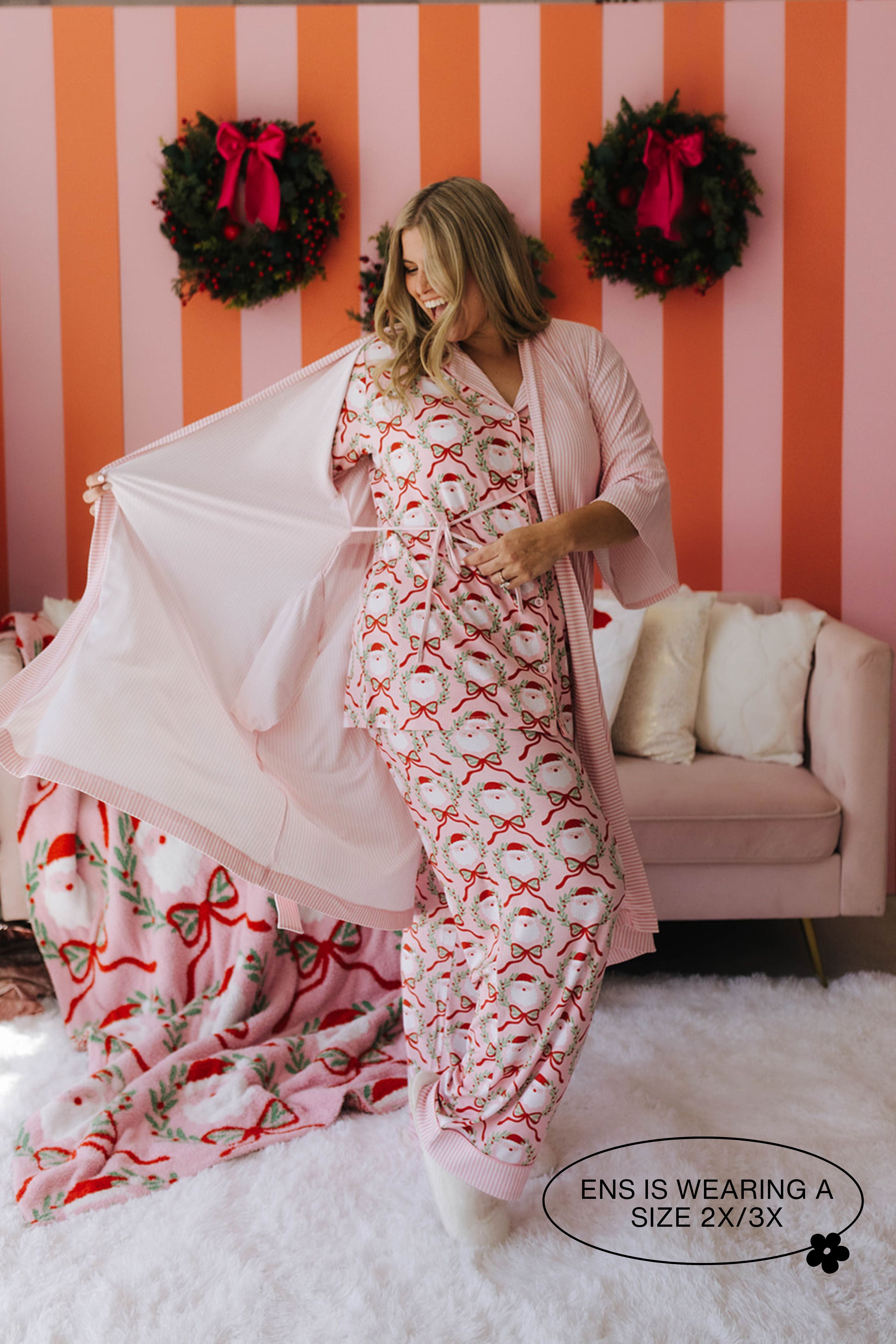 Woman wearing a festive pajama set with matching robe in a room with striped walls and wreaths.