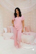 Woman wearing pink pajamas in a cozy bedroom setting with soft lighting.