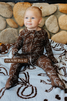 Sizing photo: Phoebe in 6-12 months wearing brown bow print baby zip pajamas.
