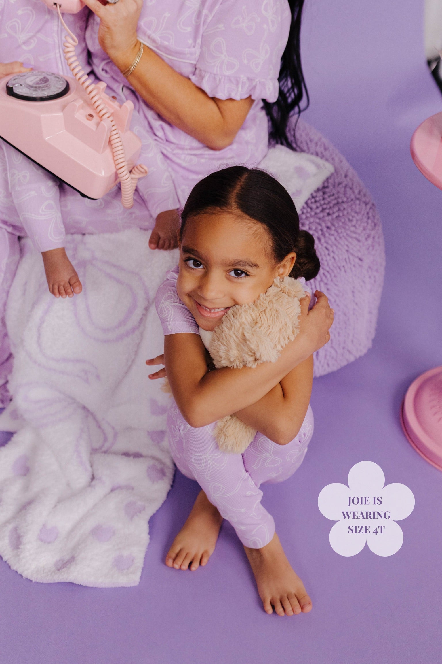 Child in a purple outfit holding a teddy bear on a purple background