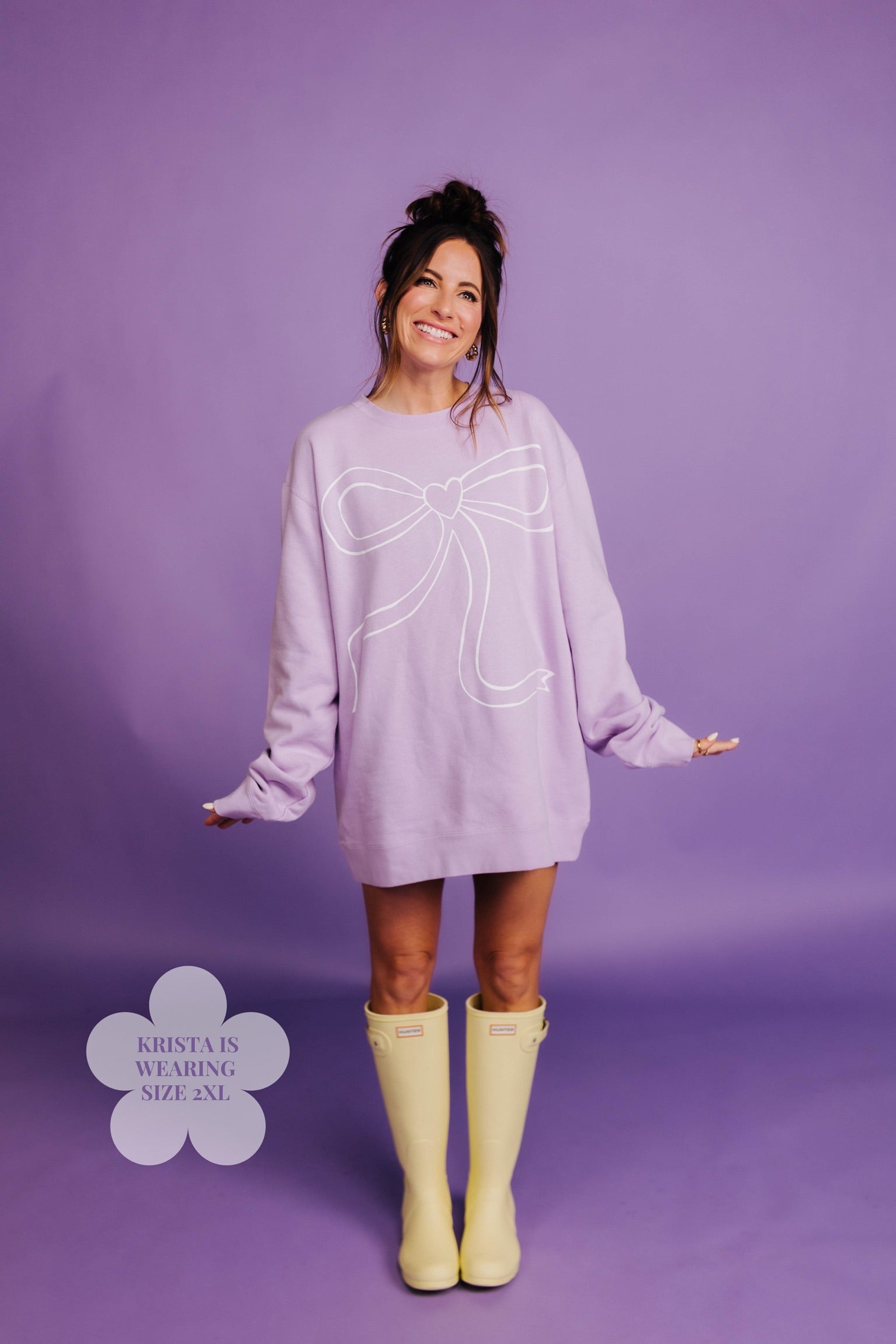 Woman wearing a light purple sweater with a large bow design on a purple background