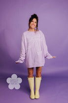 Woman wearing a light purple sweater with a large bow design on a purple background