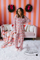 Woman wearing a pink and white patterned onesie in a cozy living room with striped walls and wreaths.