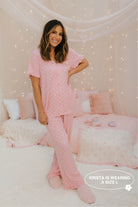 Woman wearing pink polka dot pajamas in a cozy bedroom setting.