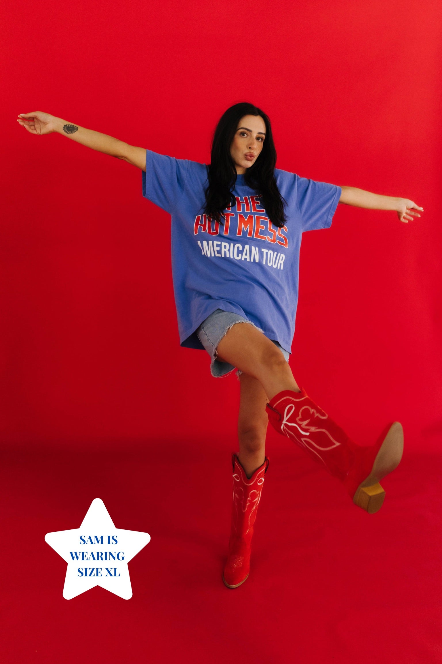 Person wearing a blue oversized t-shirt with text and red cowboy boots on a red background