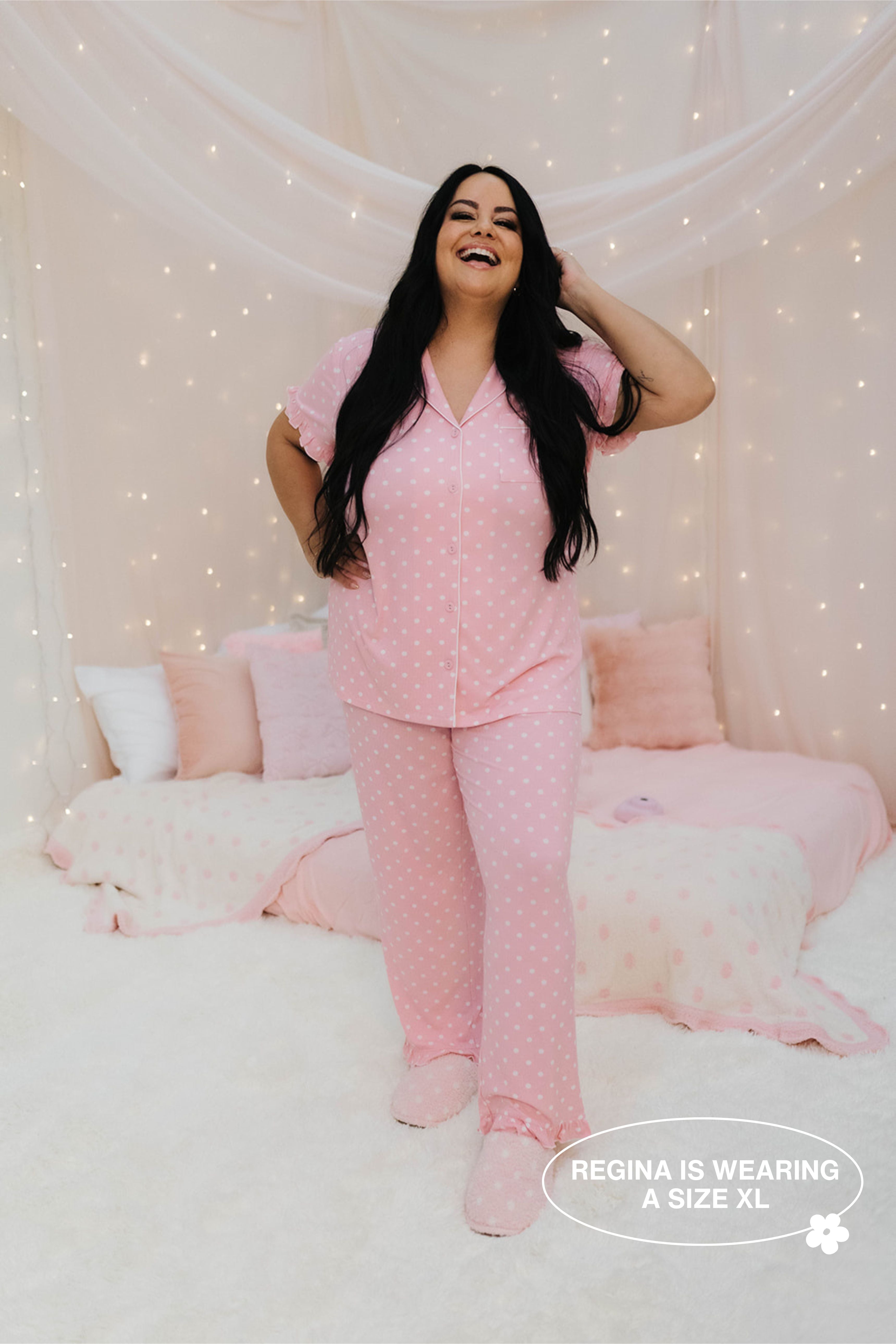 Woman wearing pink pajamas in a cozy bedroom setting with fairy lights.