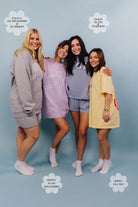 Four women posing together wearing different styles of shorts and merch on a light blue background.