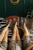 Three people wearing leopard print slippers on a patterned couch with a decorative mirror above.