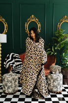 Woman wrapped in a leopard print blanket in a stylish room with green walls, gold mirrors, and patterned furniture.