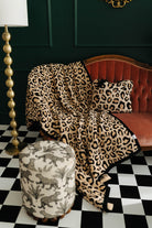 Leopard print blanket draped over a red sofa in a room with a checkered floor and lamp.